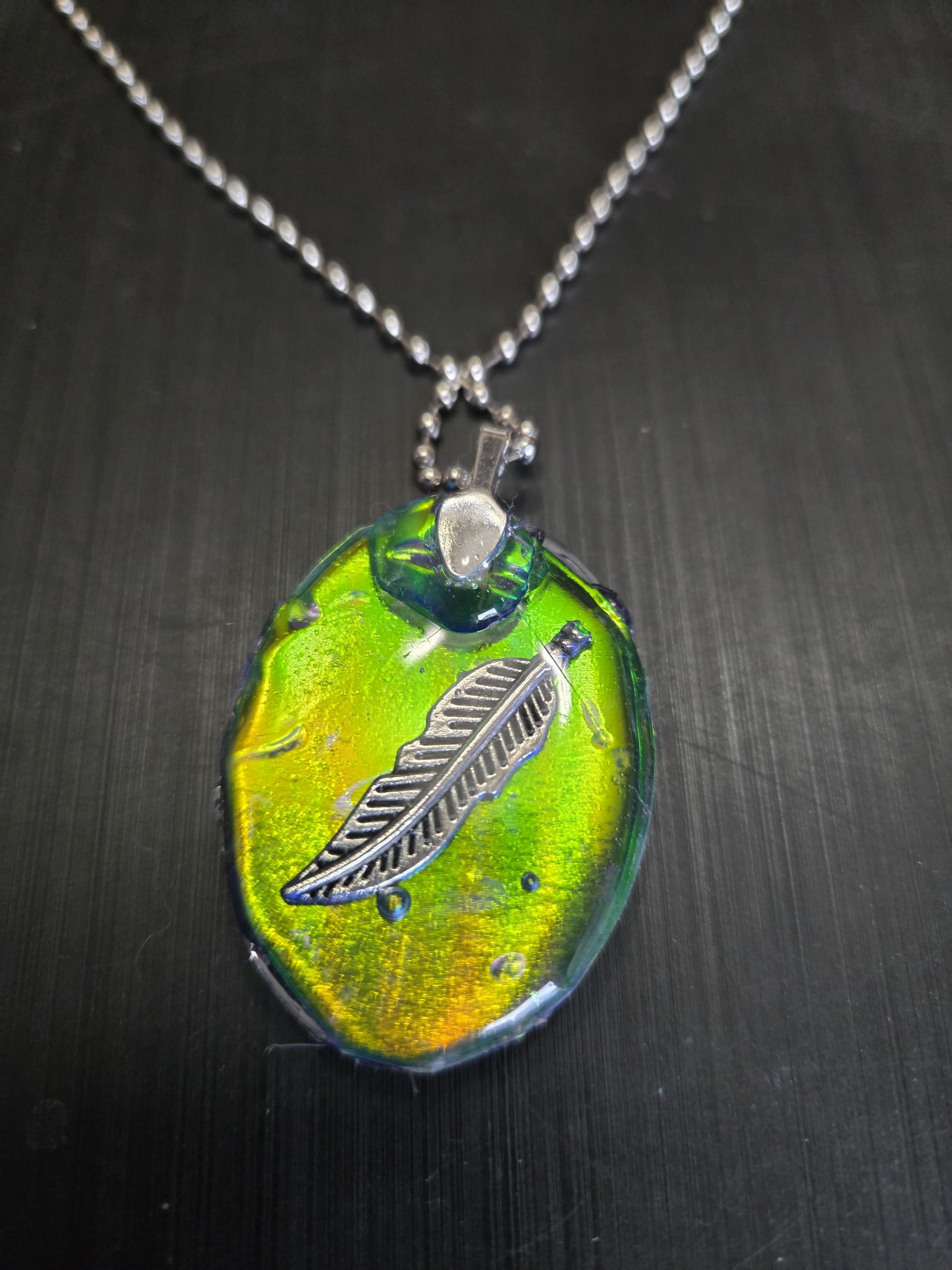 Back of the oval holographic pendant with a silver-tone feather design