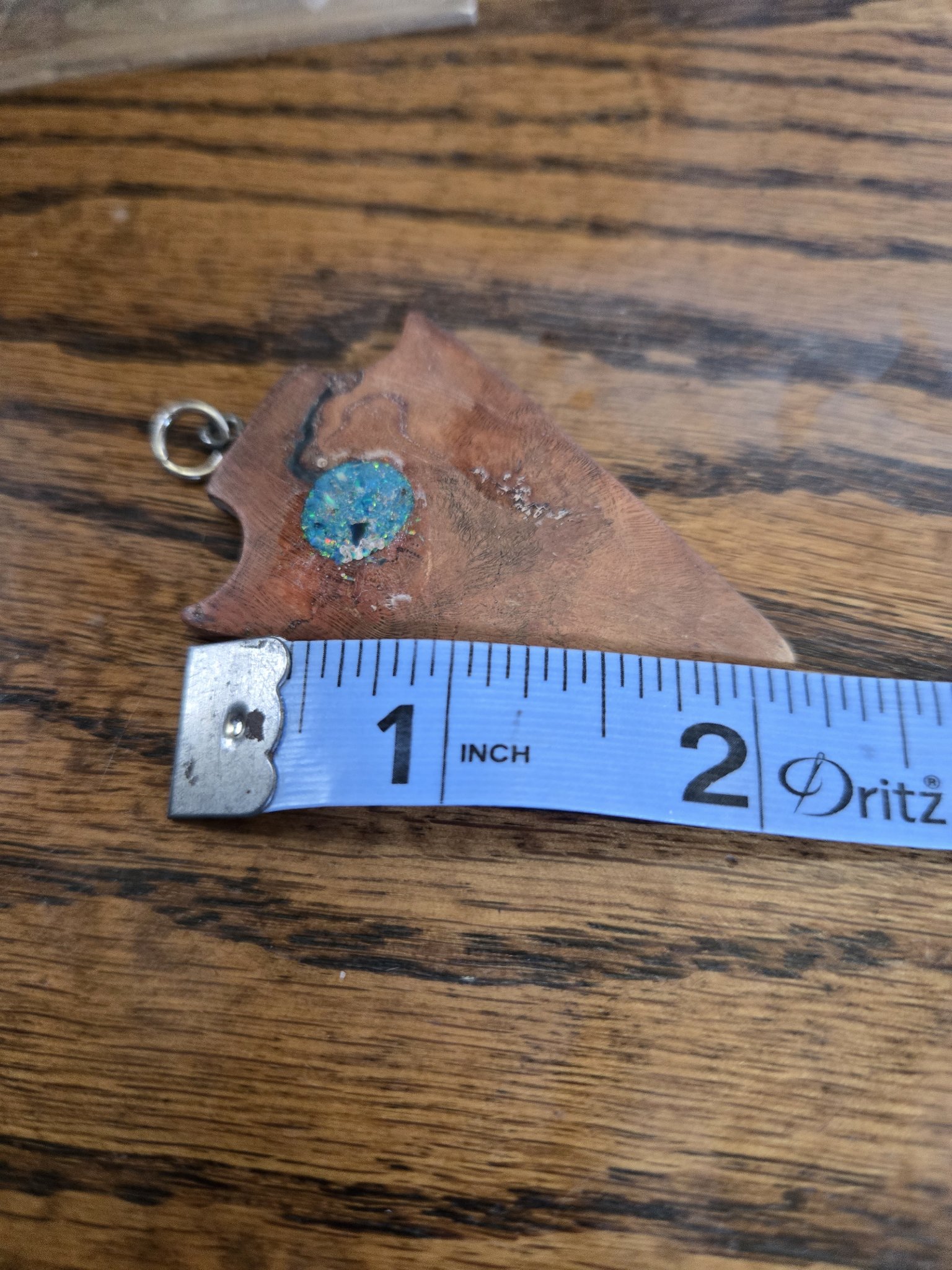 English walnut arrowhead pendant beside a tape measure showing it is about two inches wide