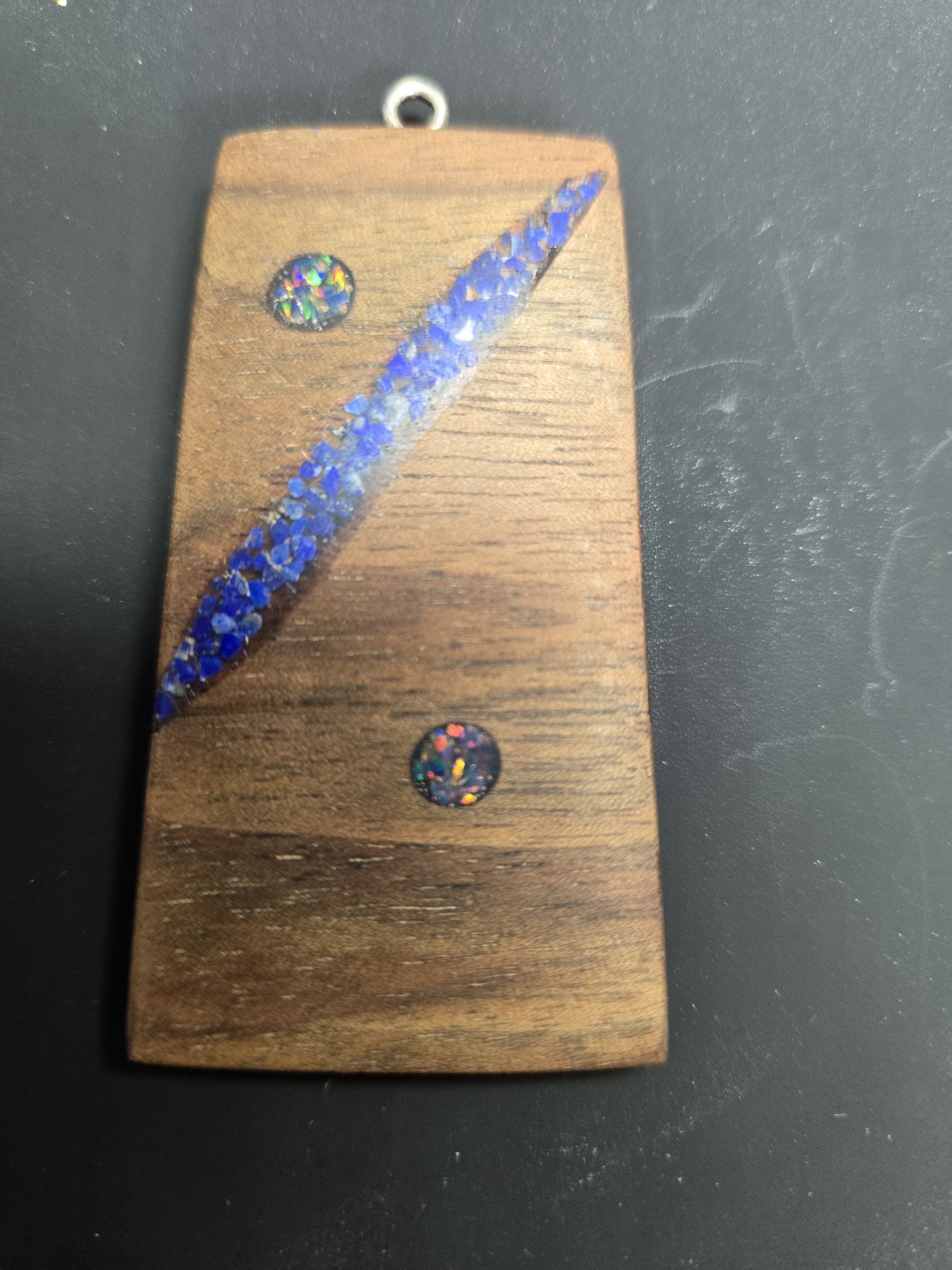 Close-up of a rectangular walnut pendant with a diagonal crushed blue lapis inlay and two round opal cabochons