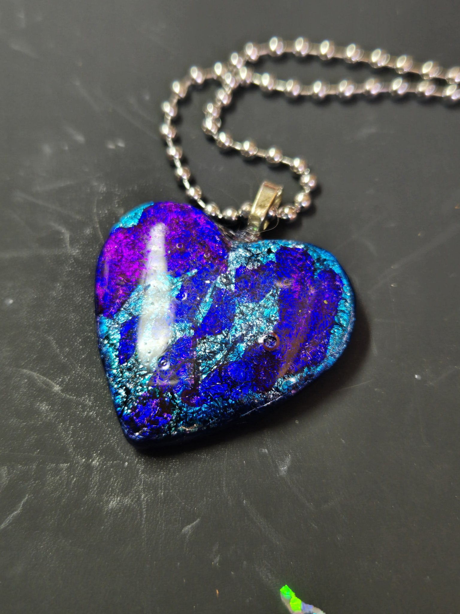 Angled close-up of the glossy resin-coated alcohol ink heart pendant and silver-tone bail