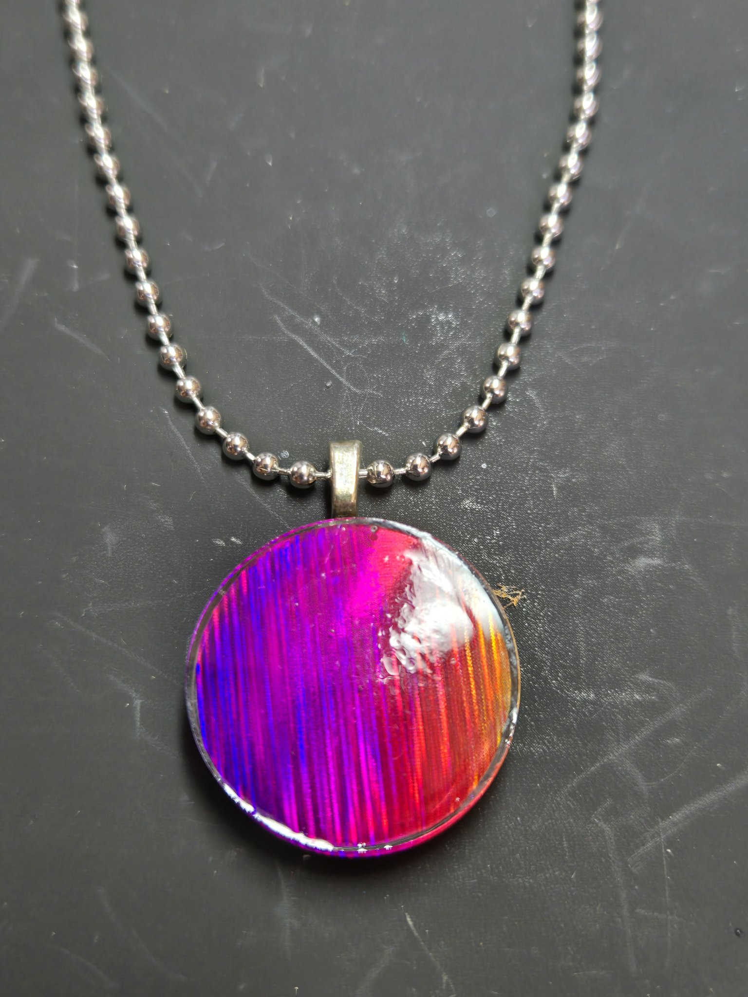 Magenta, purple, and red side of a round holographic resin pendant on a silver-tone ball chain