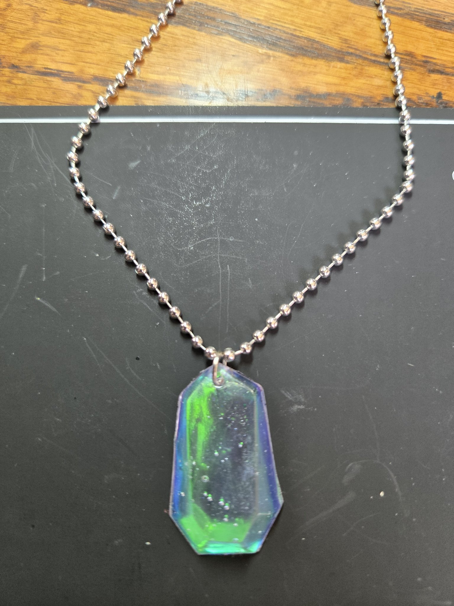 Front view of a faceted elongated-hexagon resin pendant shifting between green, blue, and purple on a silver-tone ball chain