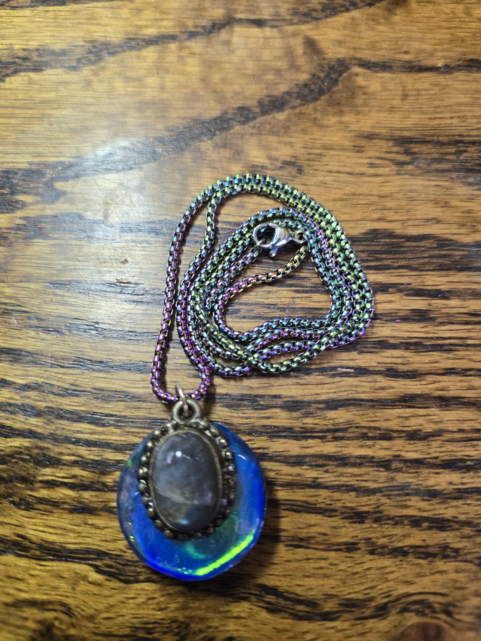 Front of an oval holographic resin pendant with a genuine labradorite cabochon in a sterling silver setting and rainbow iridescent chain