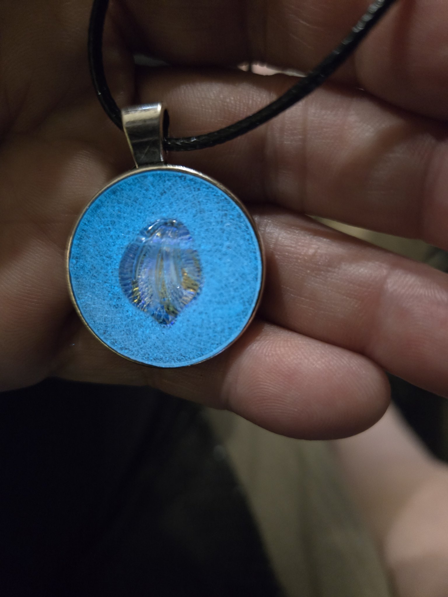Round resin shell pendant glowing bright blue while held in a hand