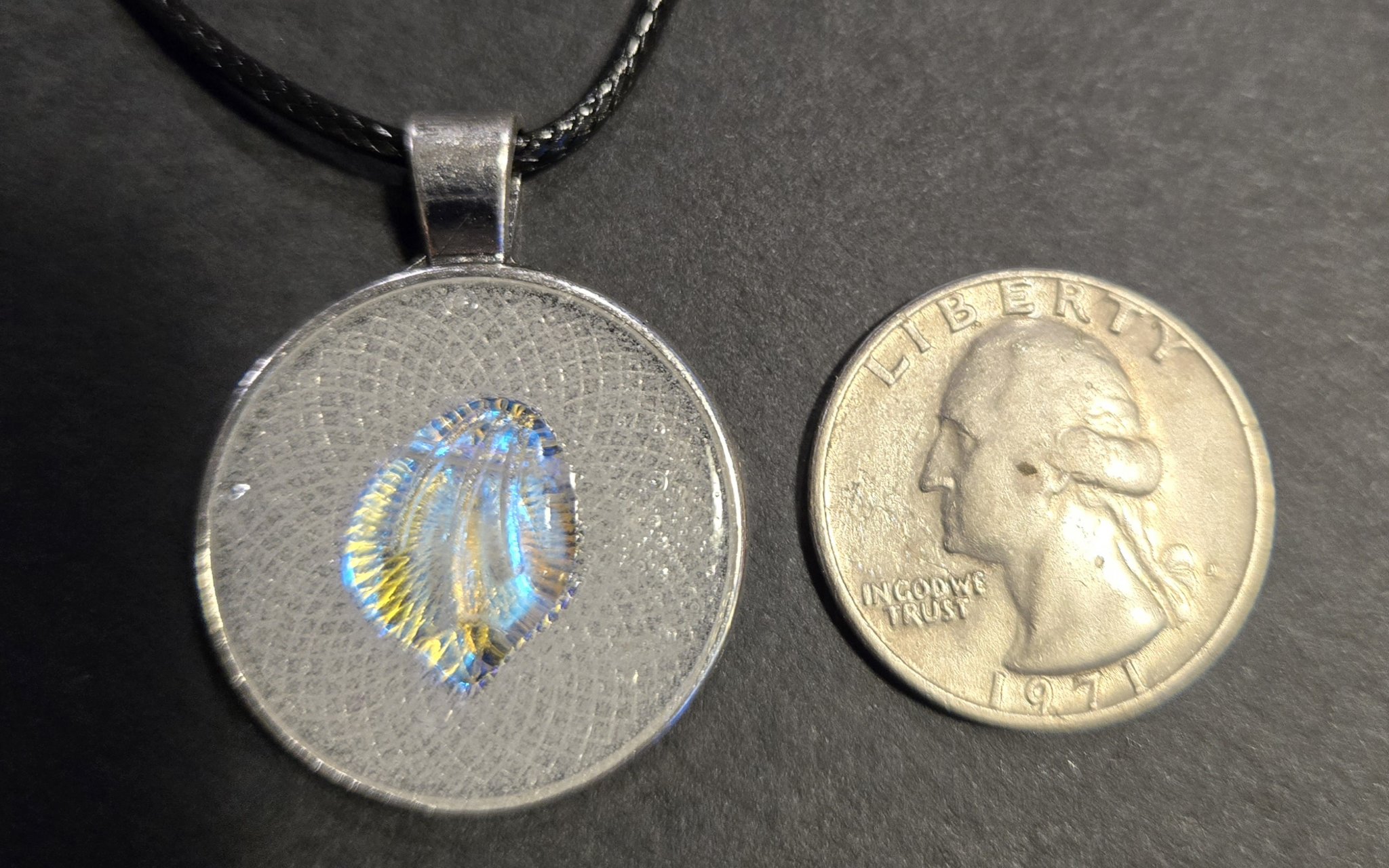 Glow-in-the-dark shell pendant beside a quarter showing its approximately one-and-a-half-inch size