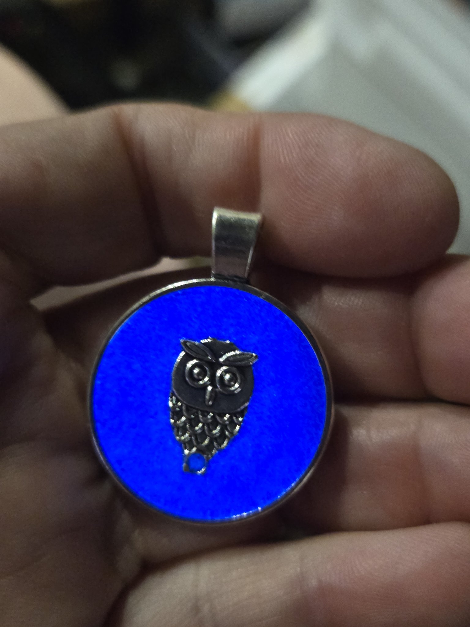 Round owl pendant glowing bright blue in a black metal frame while held in a hand