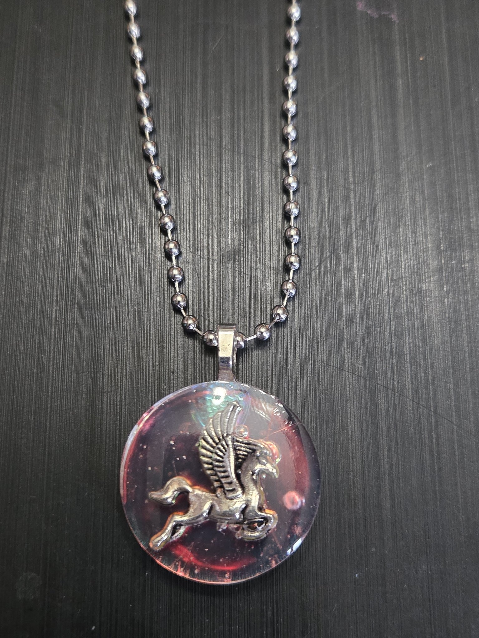 Close-up front view of the holographic resin pendant showing its silver-tone pegasus charm and shifting pink highlights