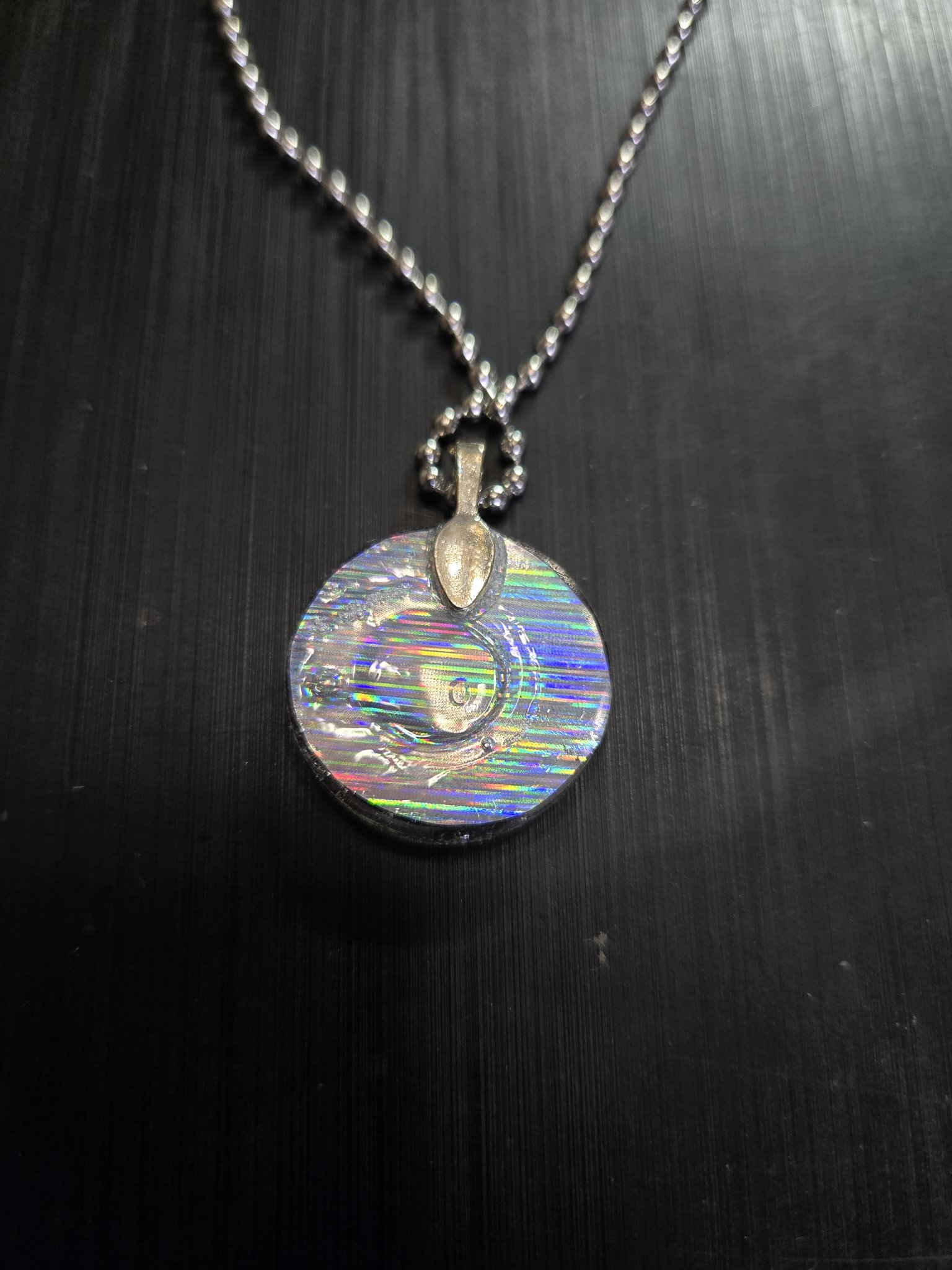 Back view of the round pendant showing its rainbow holographic finish