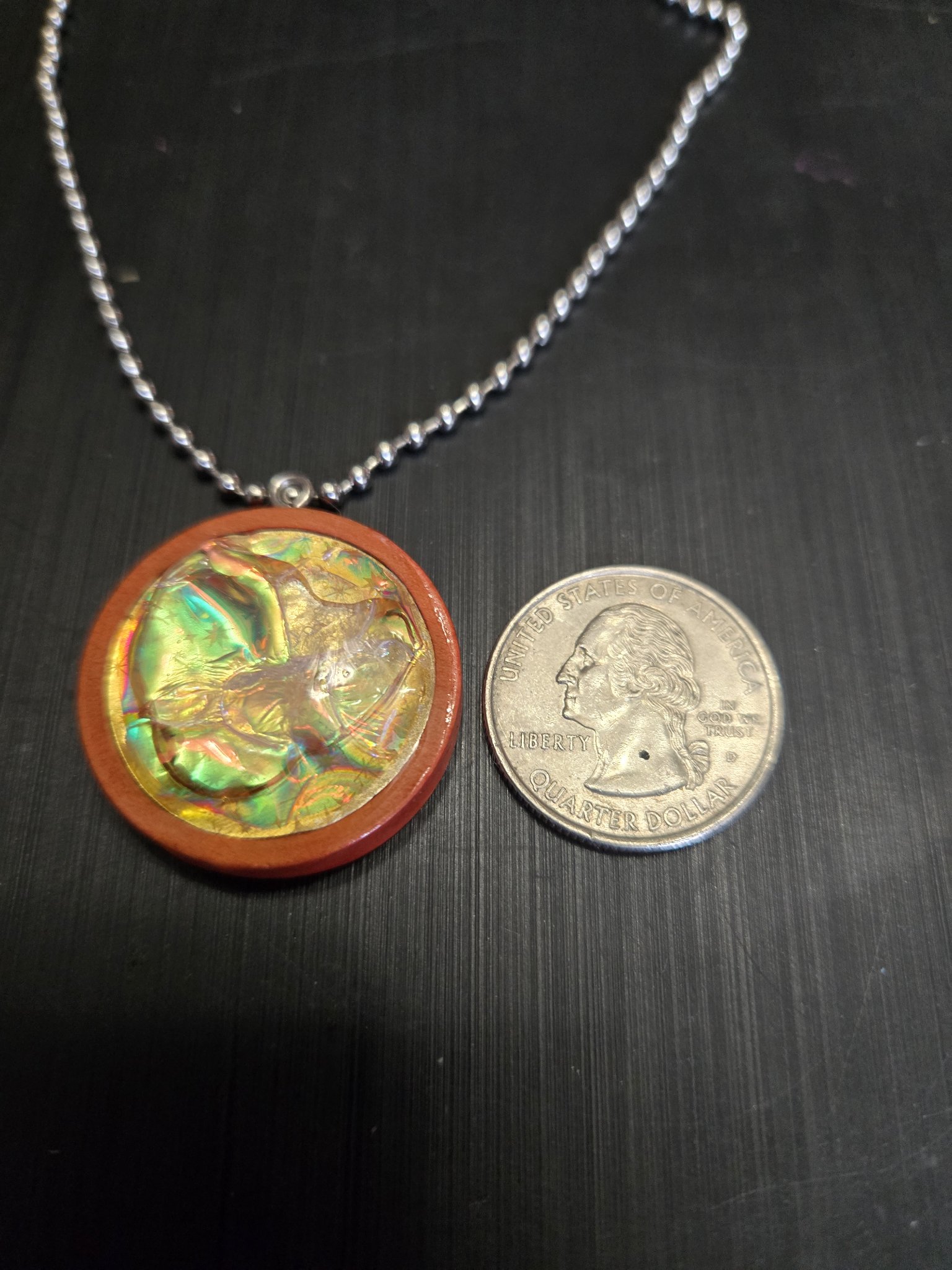 Front of the golden-green holographic pendant beside a quarter showing it is approximately one and a half inches across