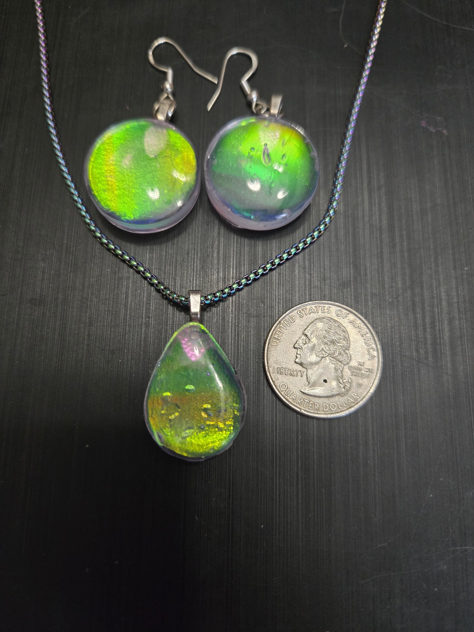 Green-gold holographic earrings and pendant beside a quarter for scale