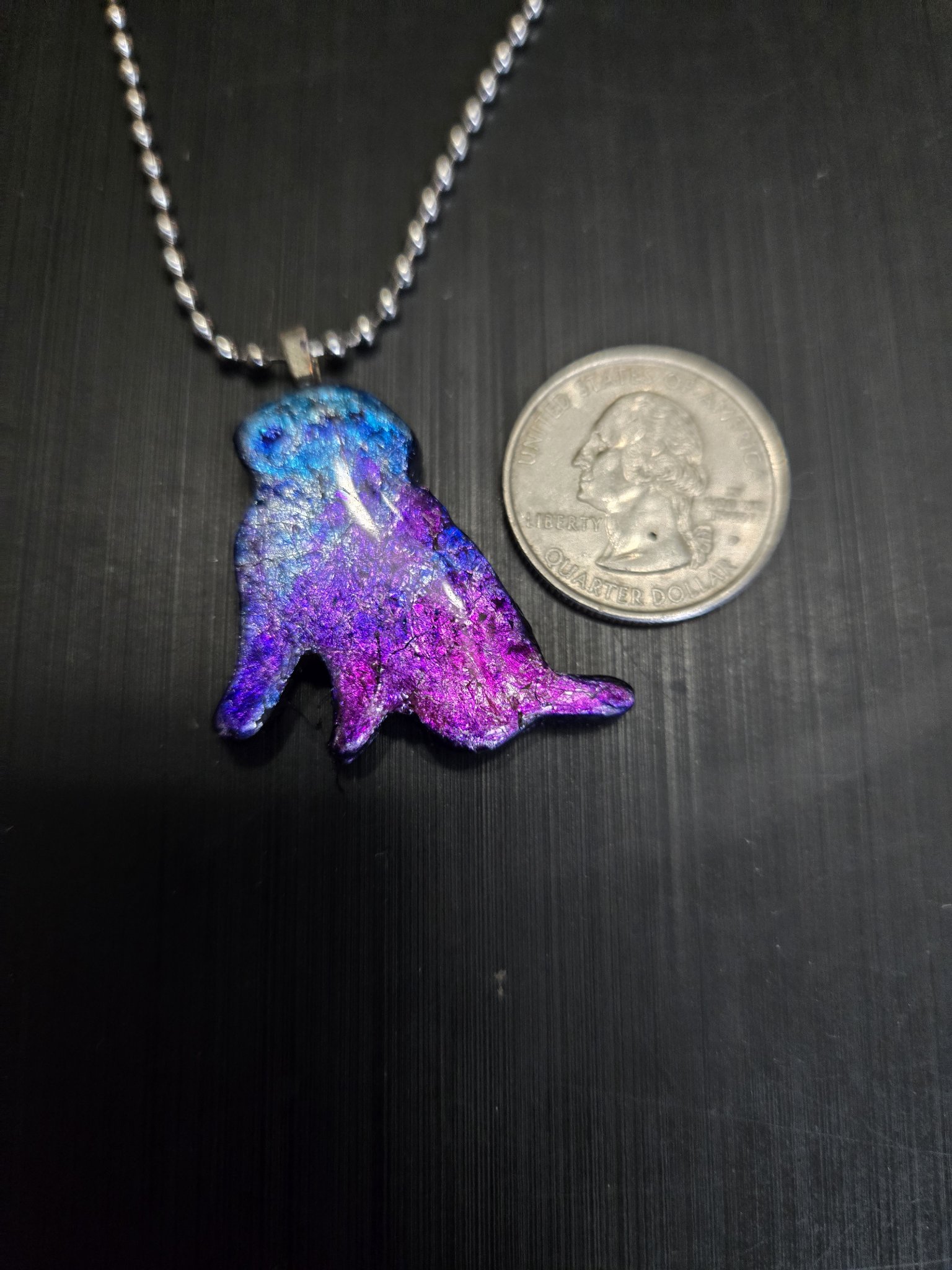 Front of the blue, purple, and pink dog-shaped polymer clay pendant beside a quarter for scale