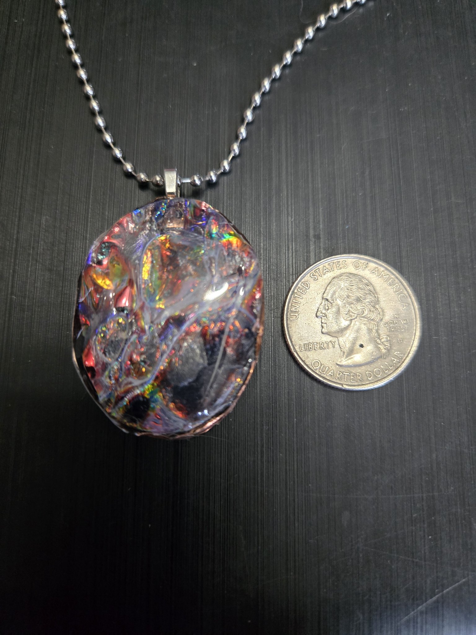 Colorful holographic front of the copper-rimmed pendant beside a quarter showing it is approximately two inches across