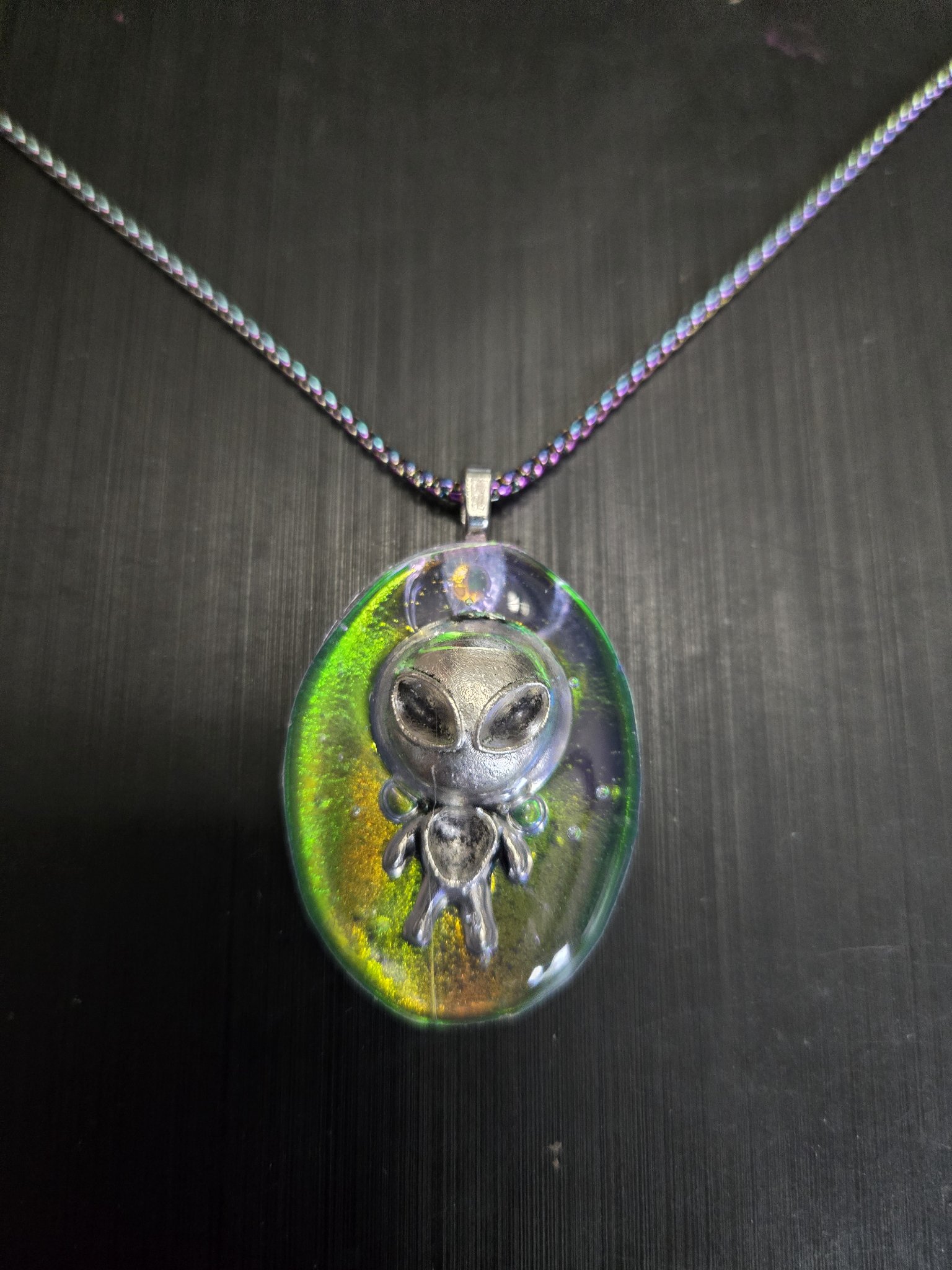 Oval green-gold holographic resin pendant with a silver-tone alien grey charm on its rainbow chain