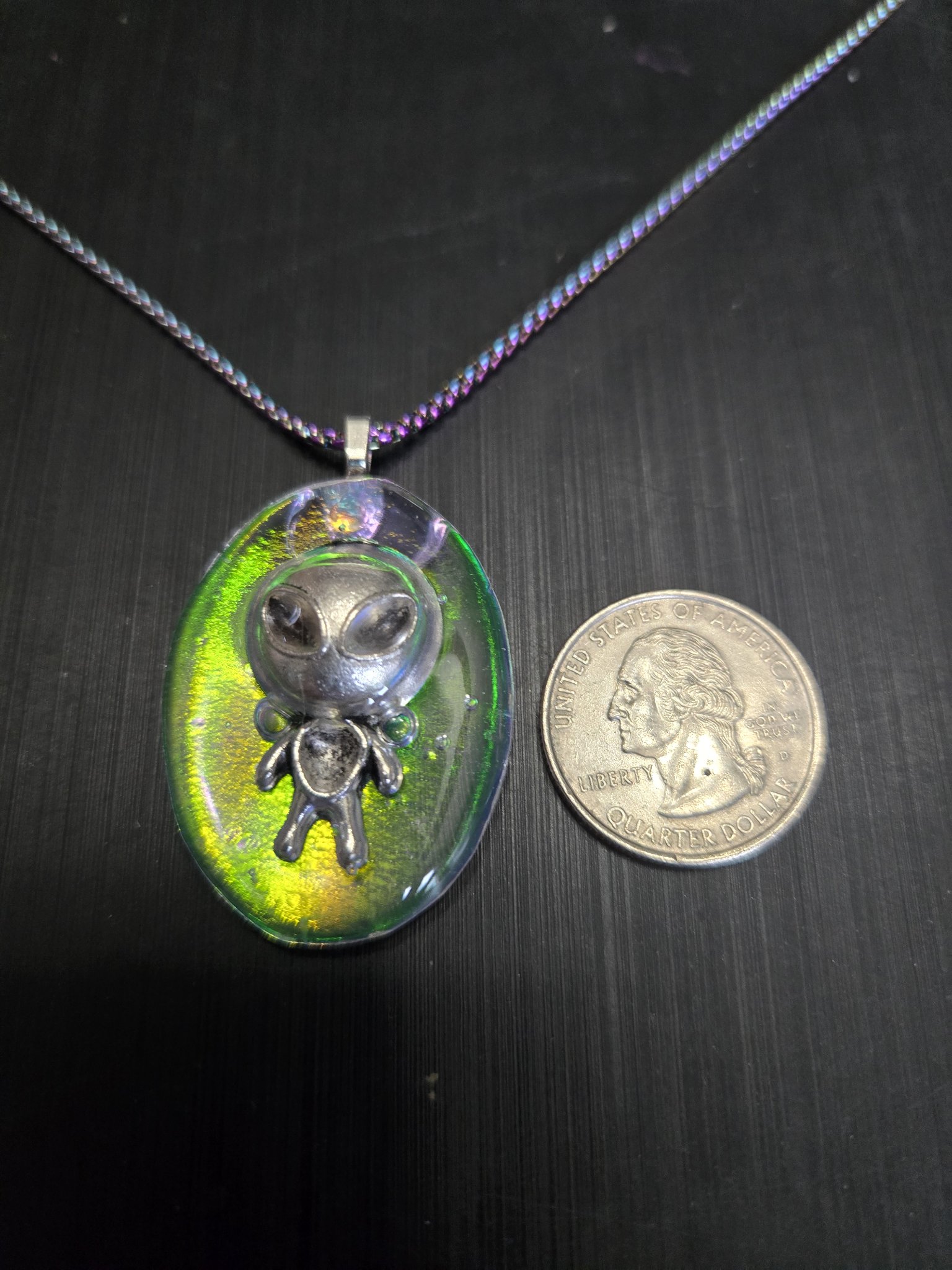 Front of the holographic alien grey pendant beside a quarter showing it is approximately two inches long