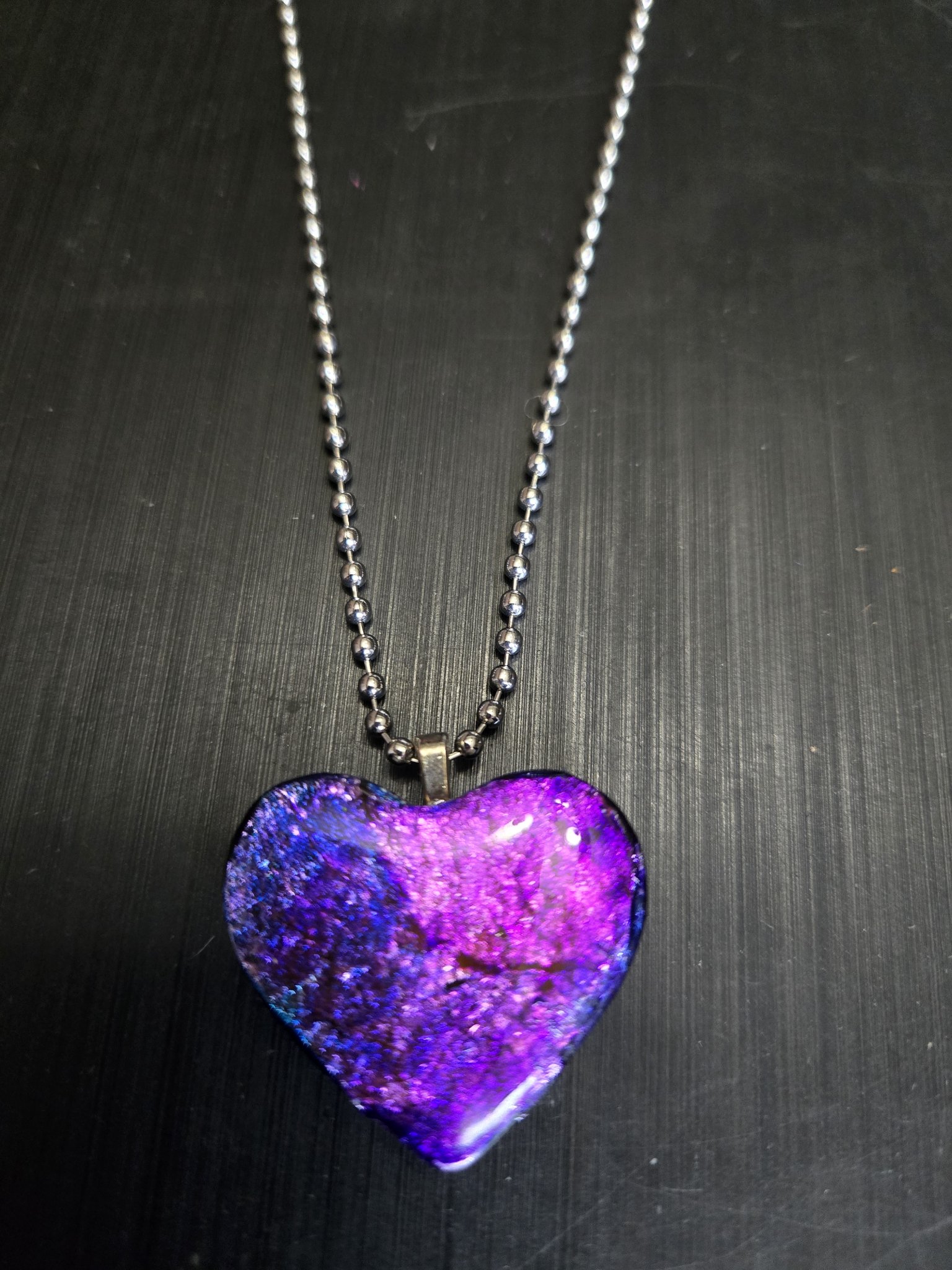 Front of the purple, blue, and pink polymer clay heart pendant with silver leaf and a glossy resin finish on its 22-inch ball chain