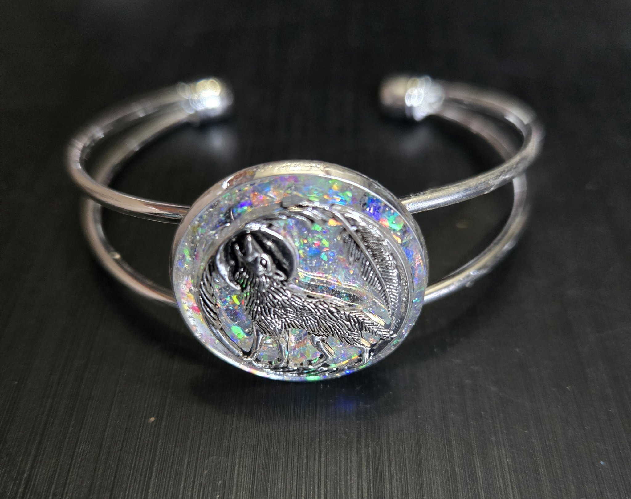 Close-up of the silver-tone adjustable cuff bracelet with a round holographic resin medallion and wolf howling at the moon design