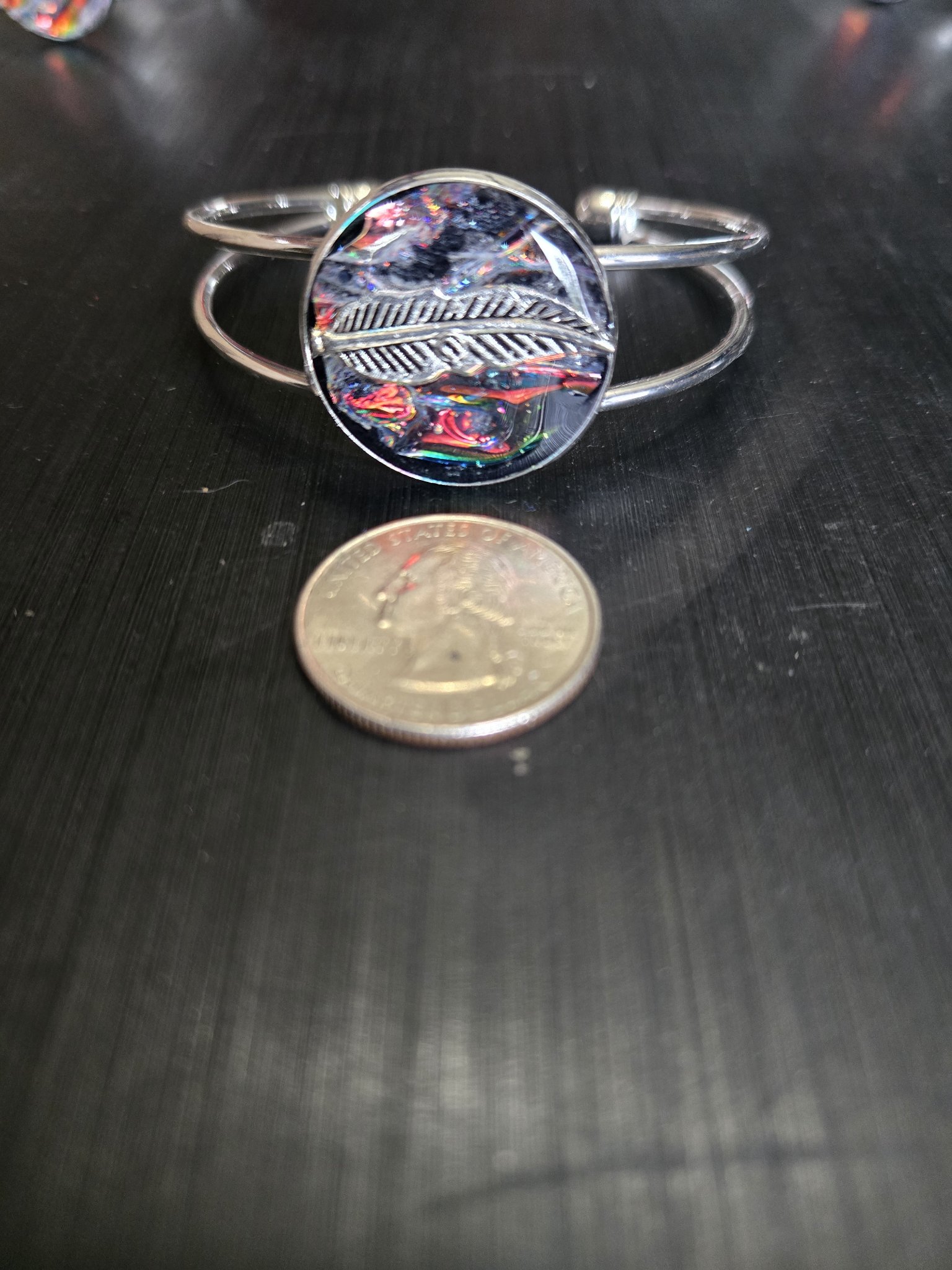 Holographic feather cuff bracelet beside a quarter showing the medallion is approximately one and a half inches across