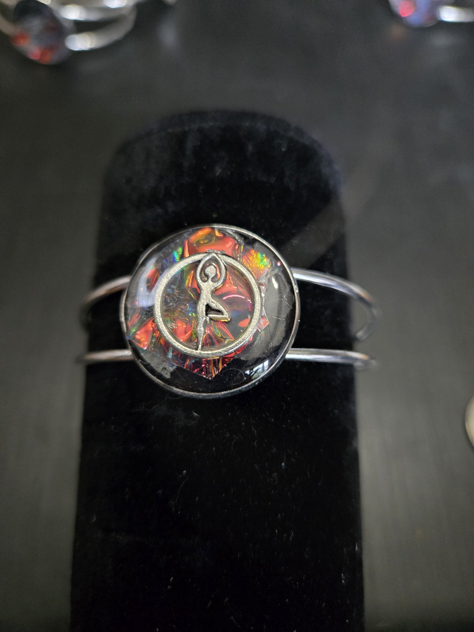 Silver-tone adjustable cuff bracelet on a black display stand with a dancer over a colorful holographic resin medallion