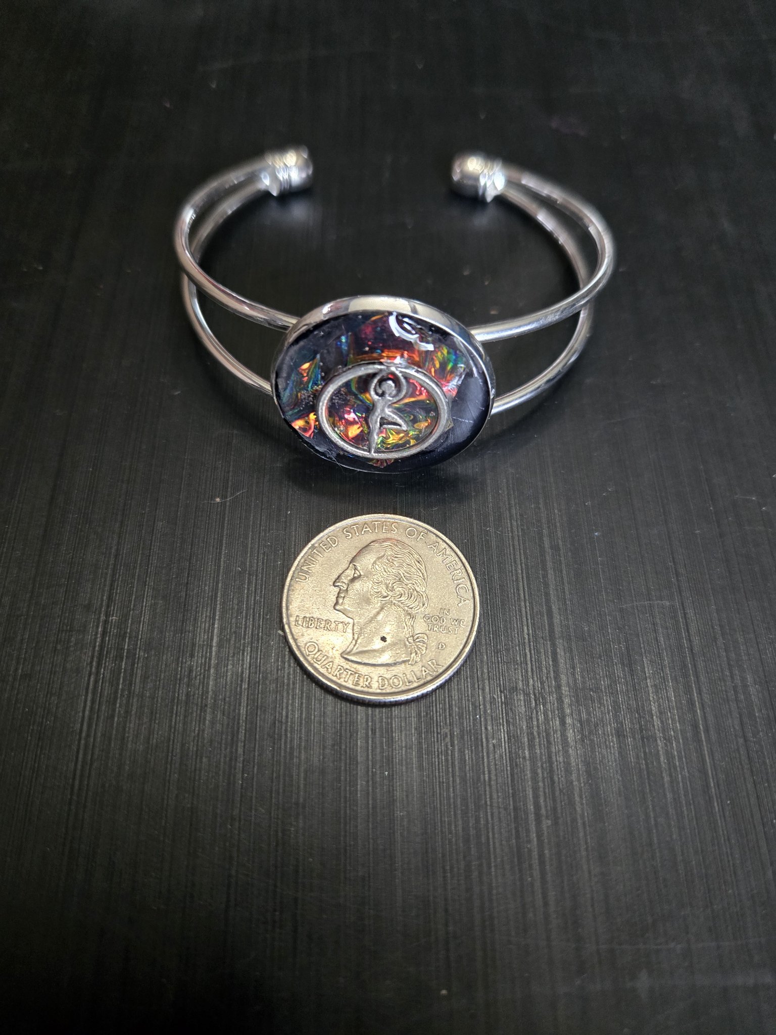 Alternate close-up of the silver-tone adjustable cuff bracelet and dancer medallion beside a quarter