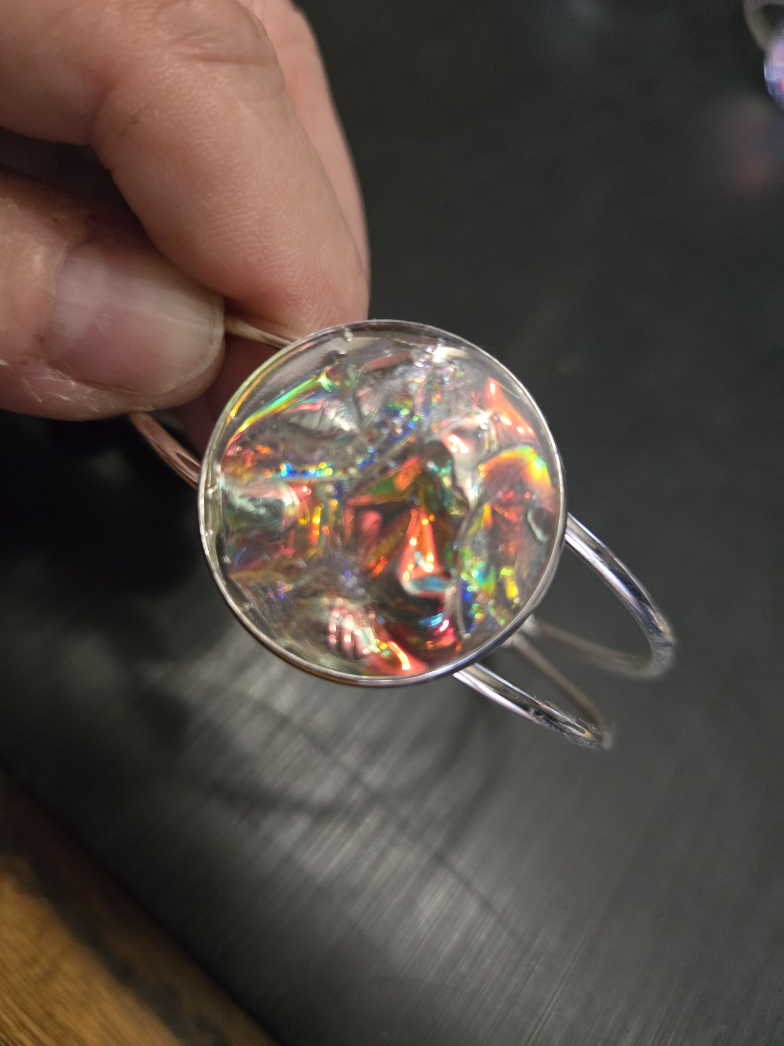 Silver-tone adjustable cuff bracelet held in a hand with a plain colorful holographic resin medallion