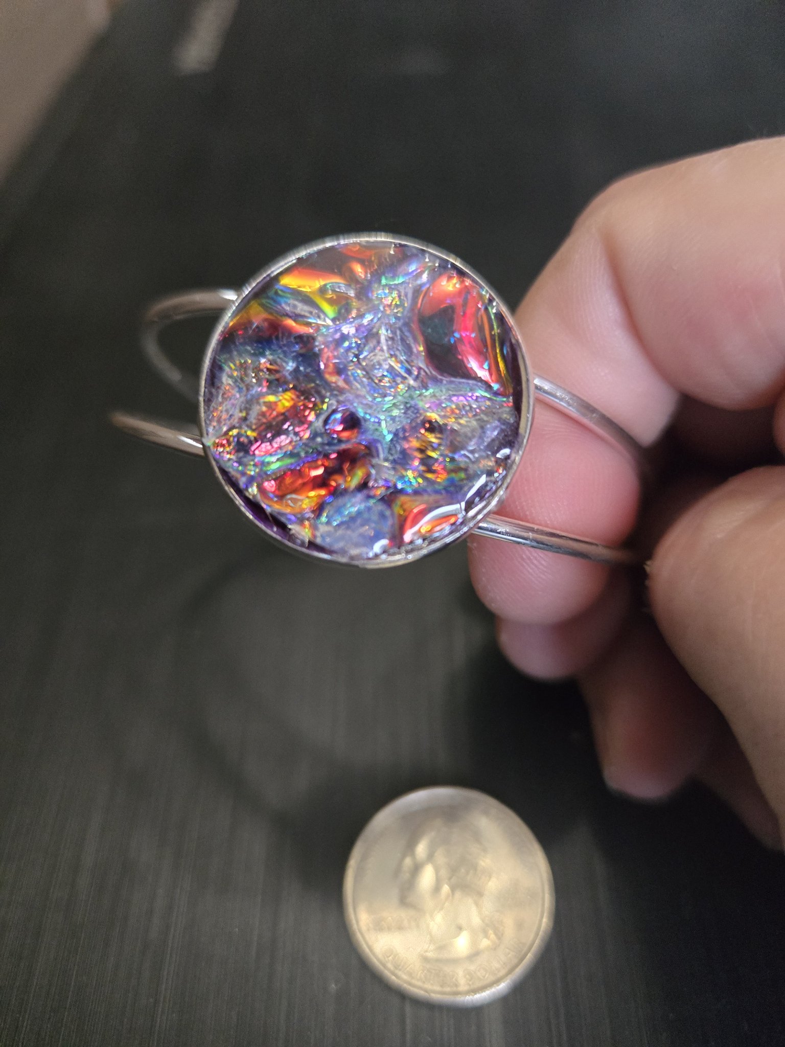 Stock 143 silver-tone adjustable cuff bracelet held in a hand with a plain holographic resin medallion beside a quarter