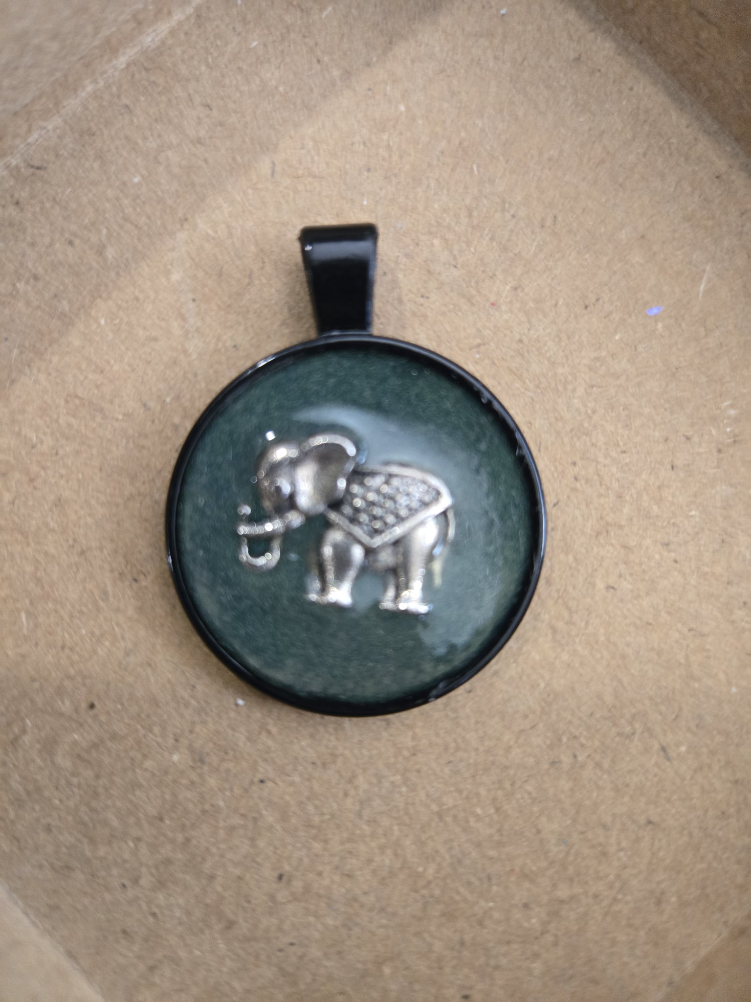 Stock 168 round green resin pendant in a black metal frame with a silver-tone elephant charm in daylight