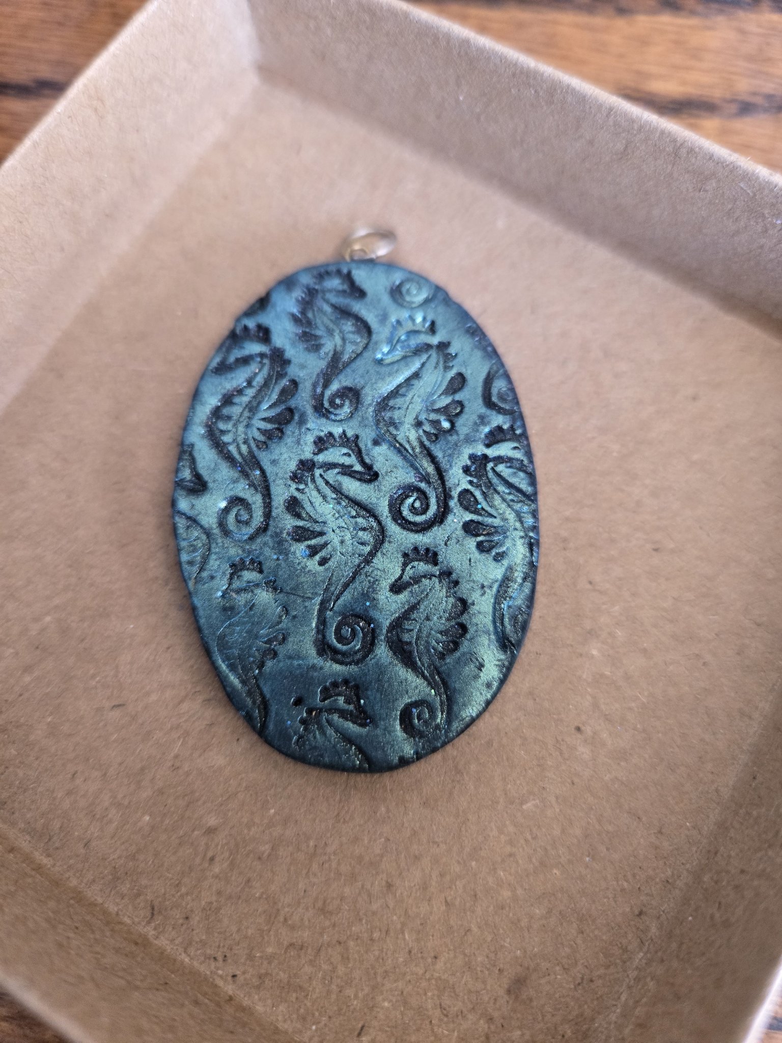 Stock 171 oval teal blue polymer clay pendant with stamped seahorse designs, shown in a front close-up