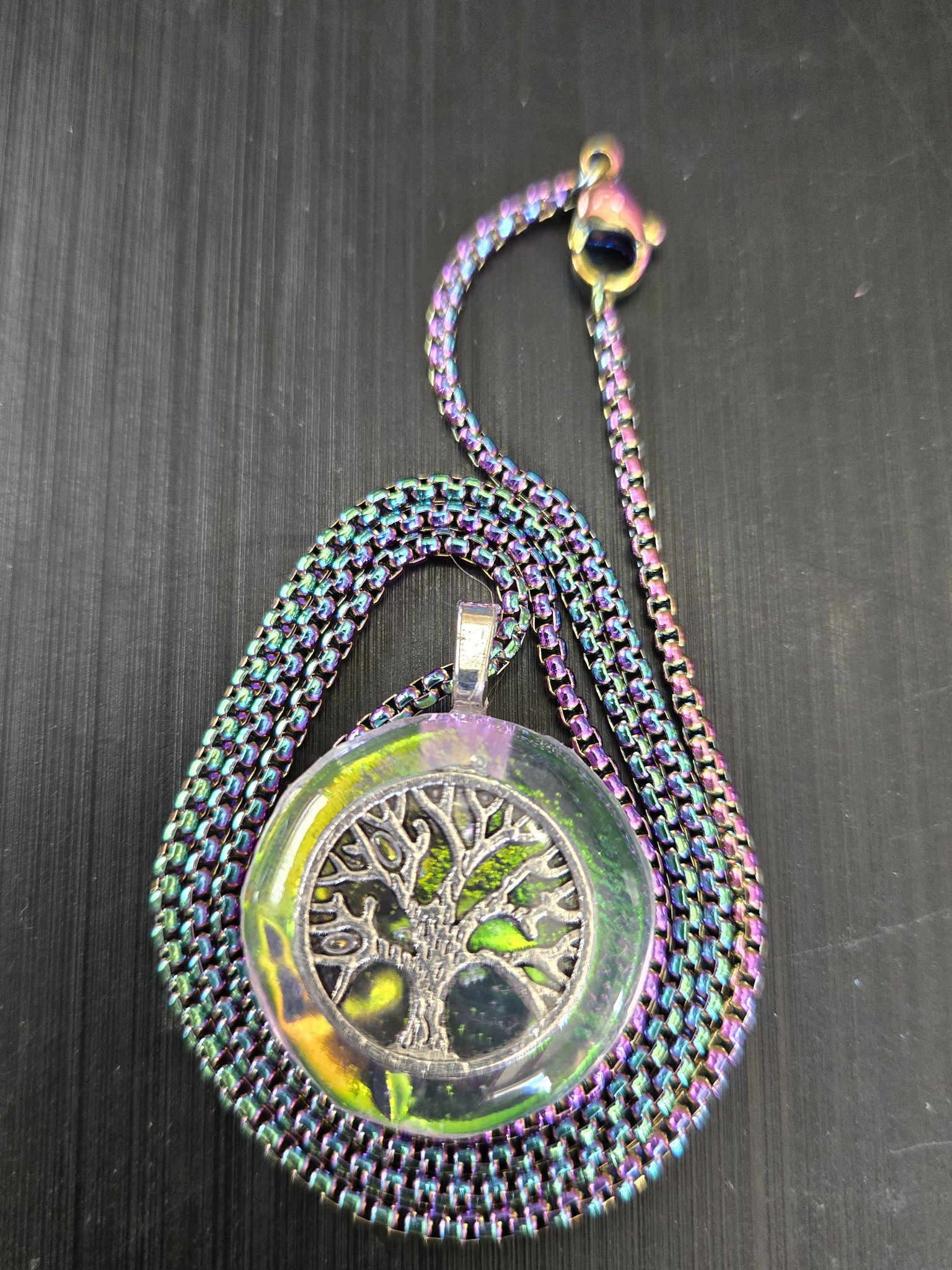 Front view of stock 182 holographic tree of life resin pendant with its 20-inch rainbow chain coiled beside it