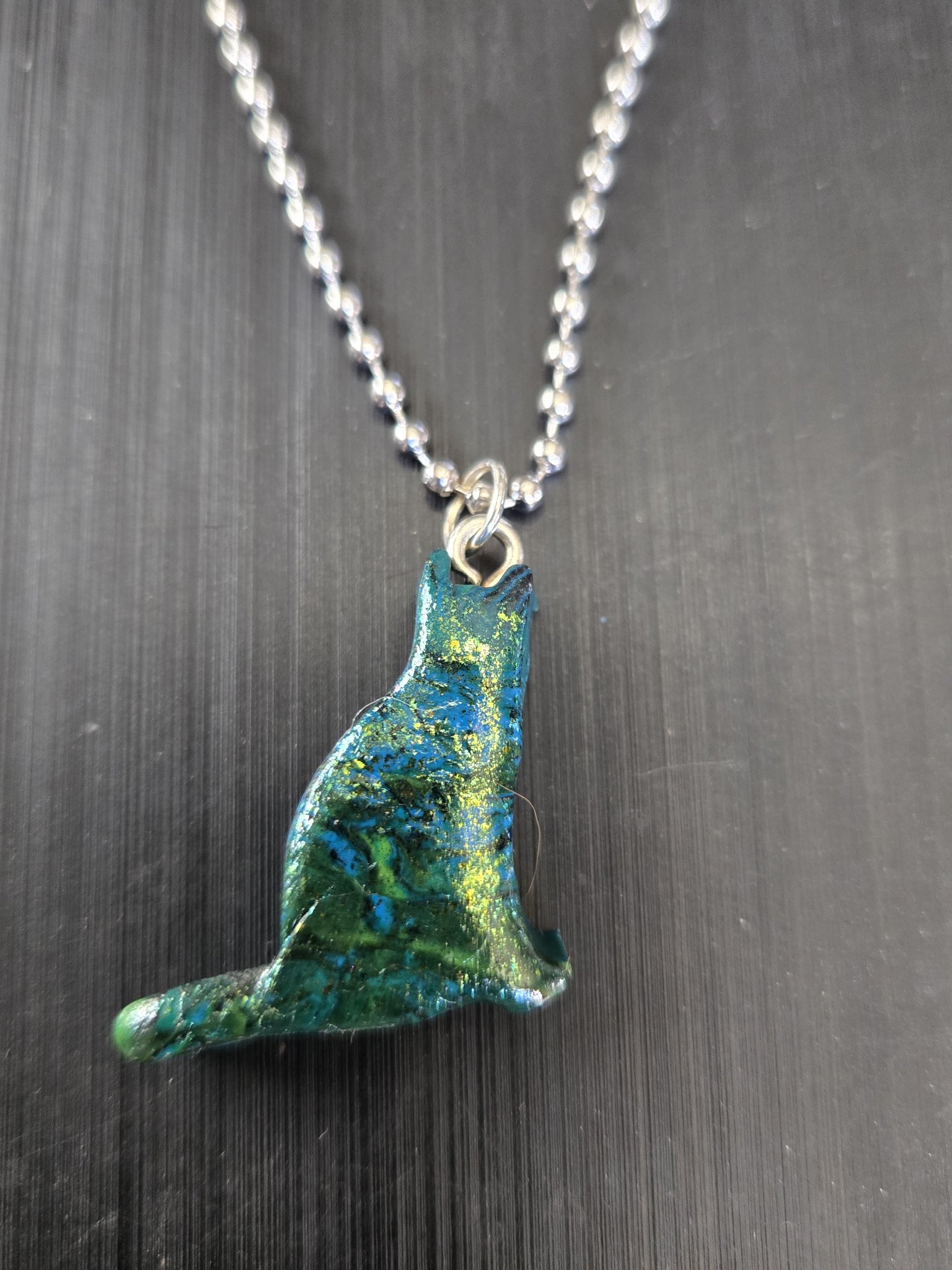 Stock 183 sitting cat pendant in polymer clay with a blue, green, and gold mica sheen, shown in a front close-up