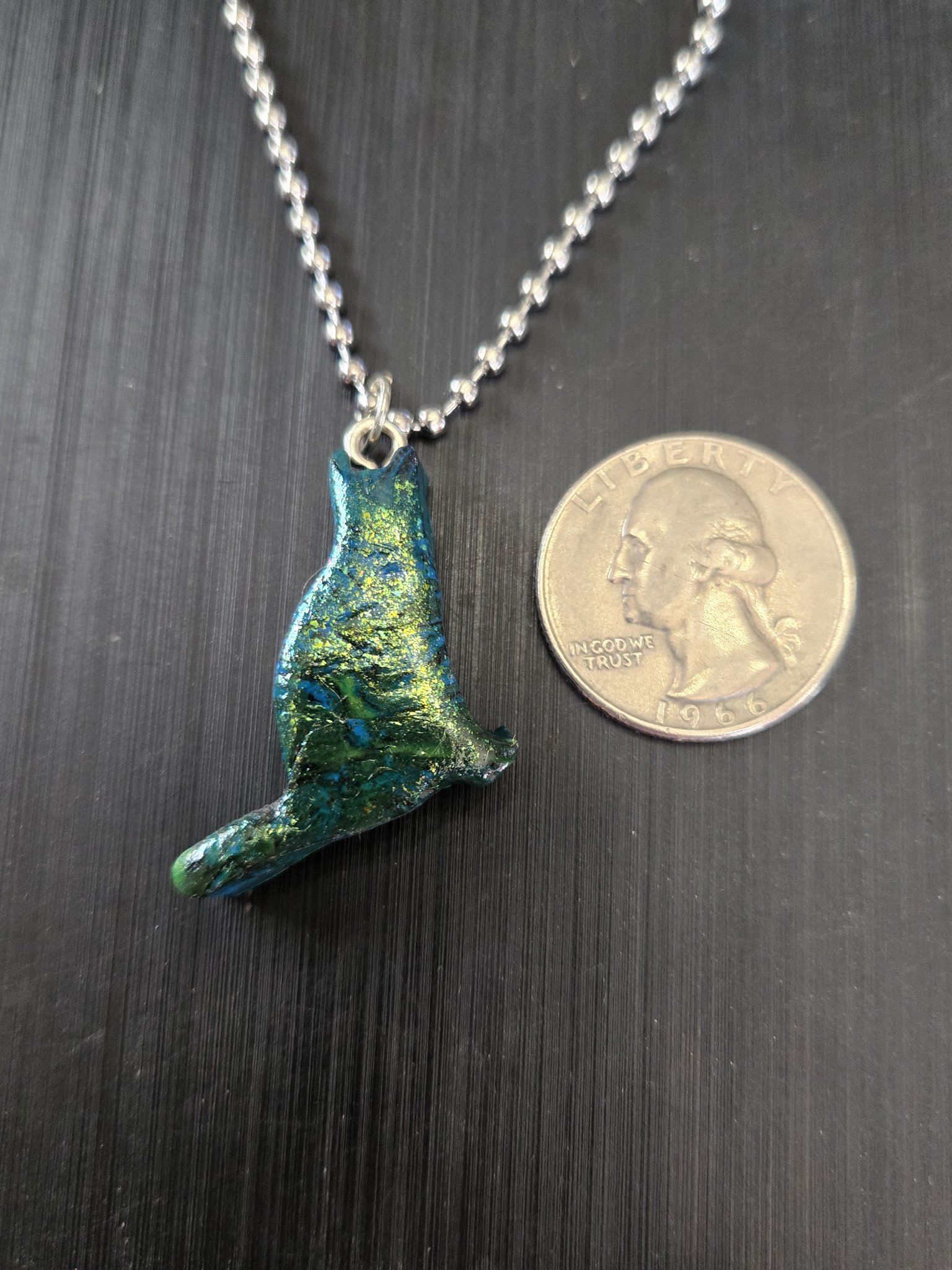 Front of stock 183 mica sheen polymer clay cat pendant beside a quarter for scale