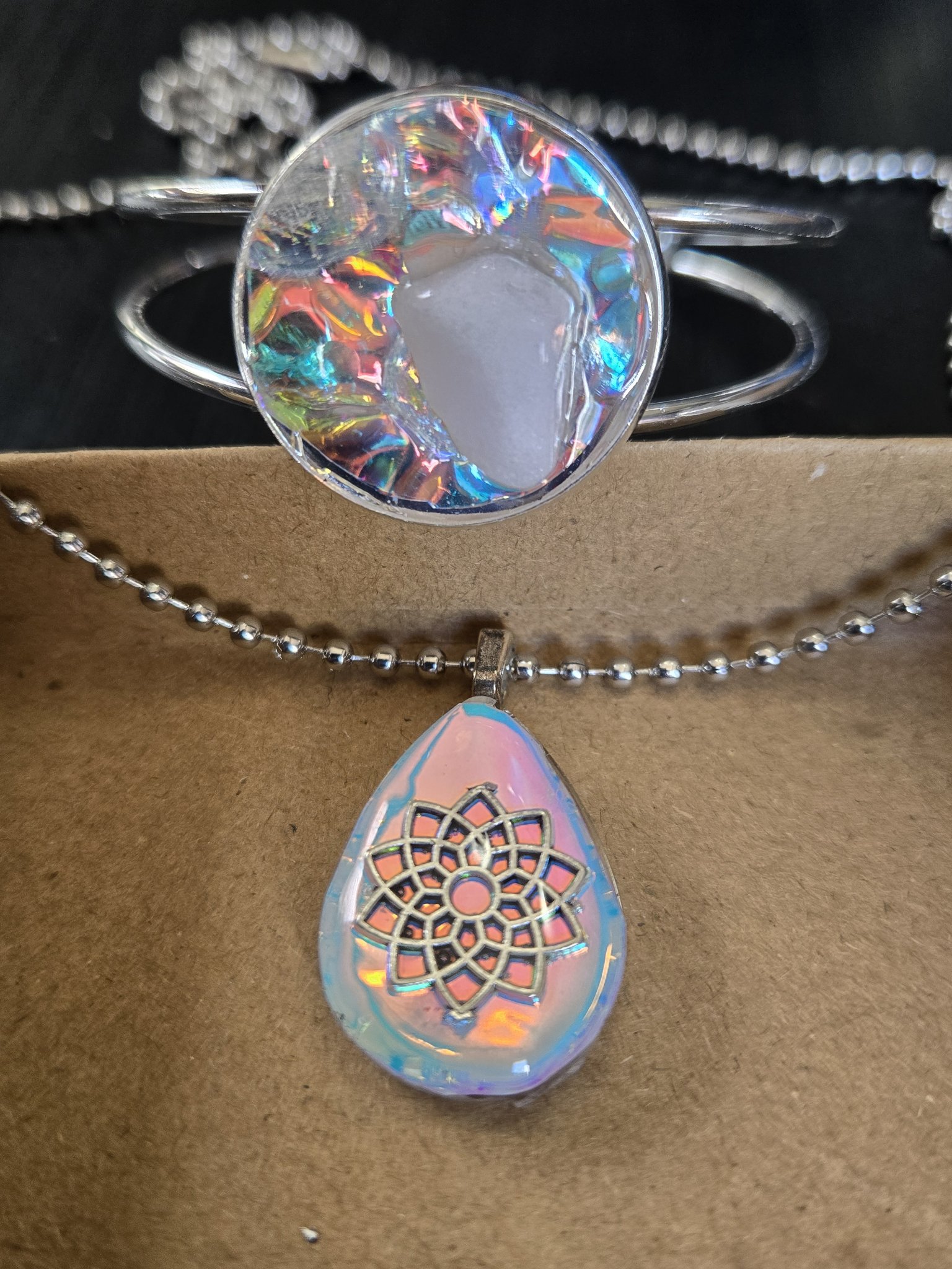 Stock 184 holographic set with adjustable silver-tone quartz cuff bracelet and pink-blue teardrop flower of life pendant shown together in close-up