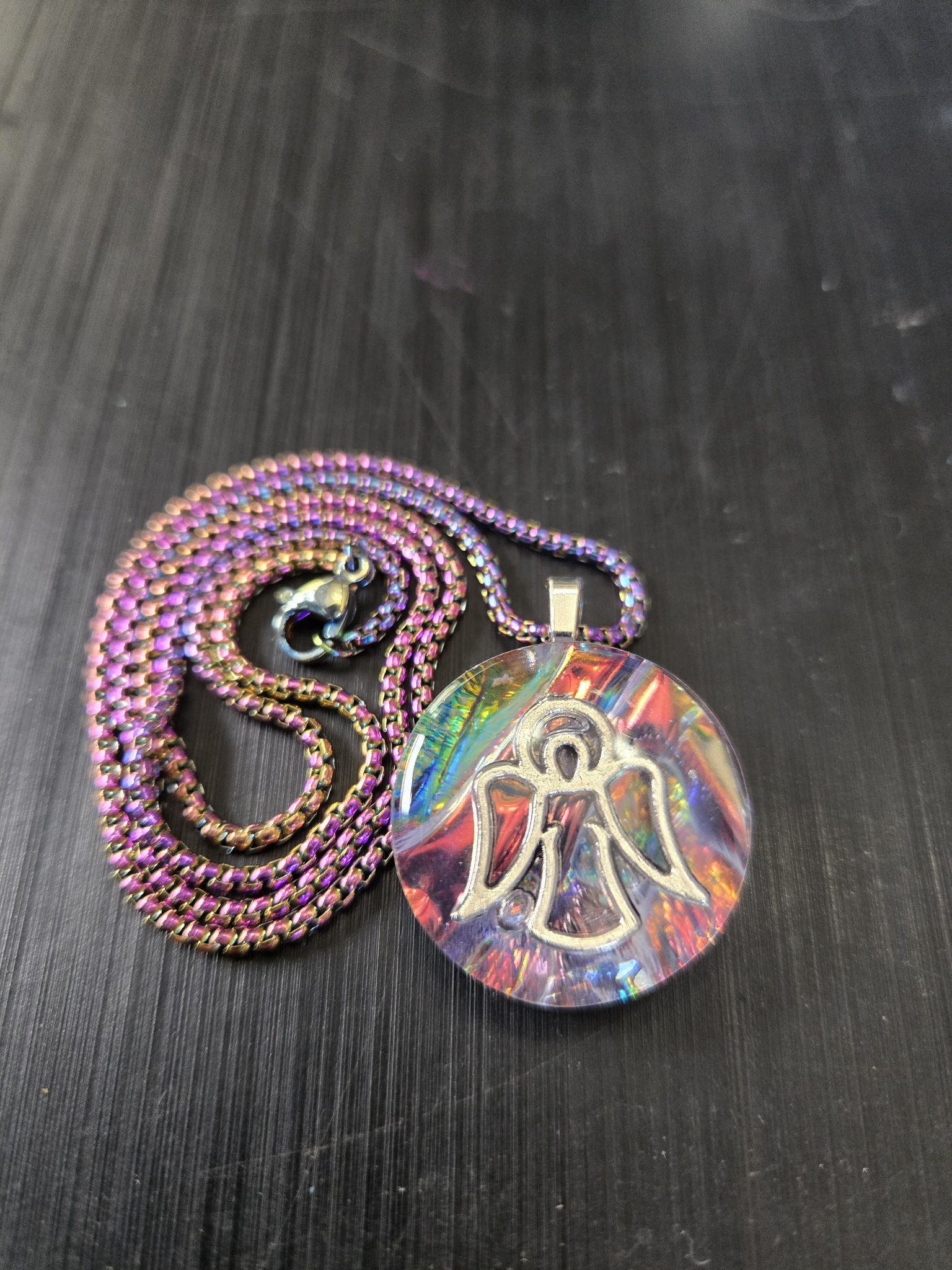 Front close-up of stock 191 round rainbow-iridescent holographic resin pendant with a silver-tone angel charm