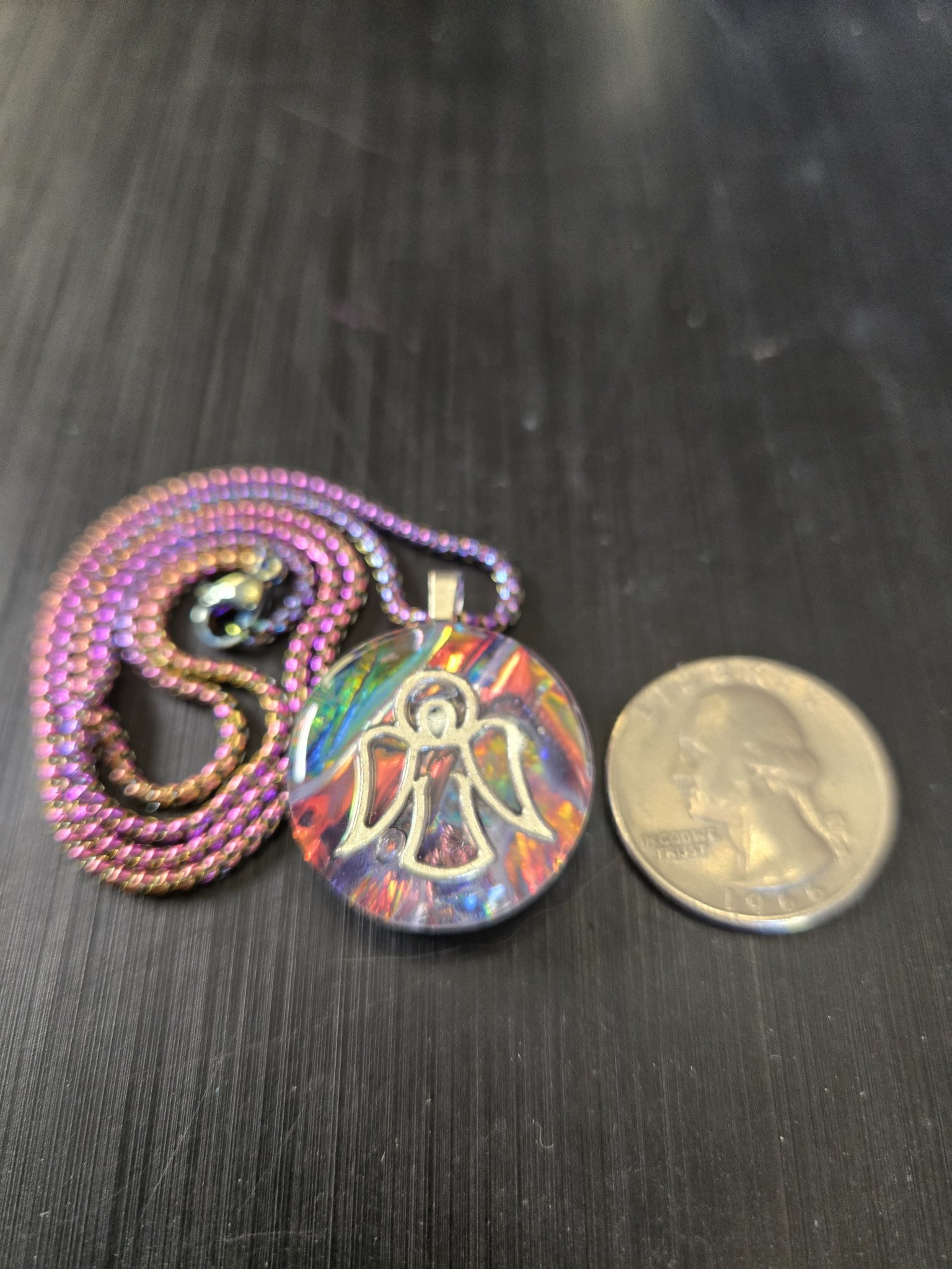 Front of stock 191 holographic angel resin pendant beside a quarter for scale