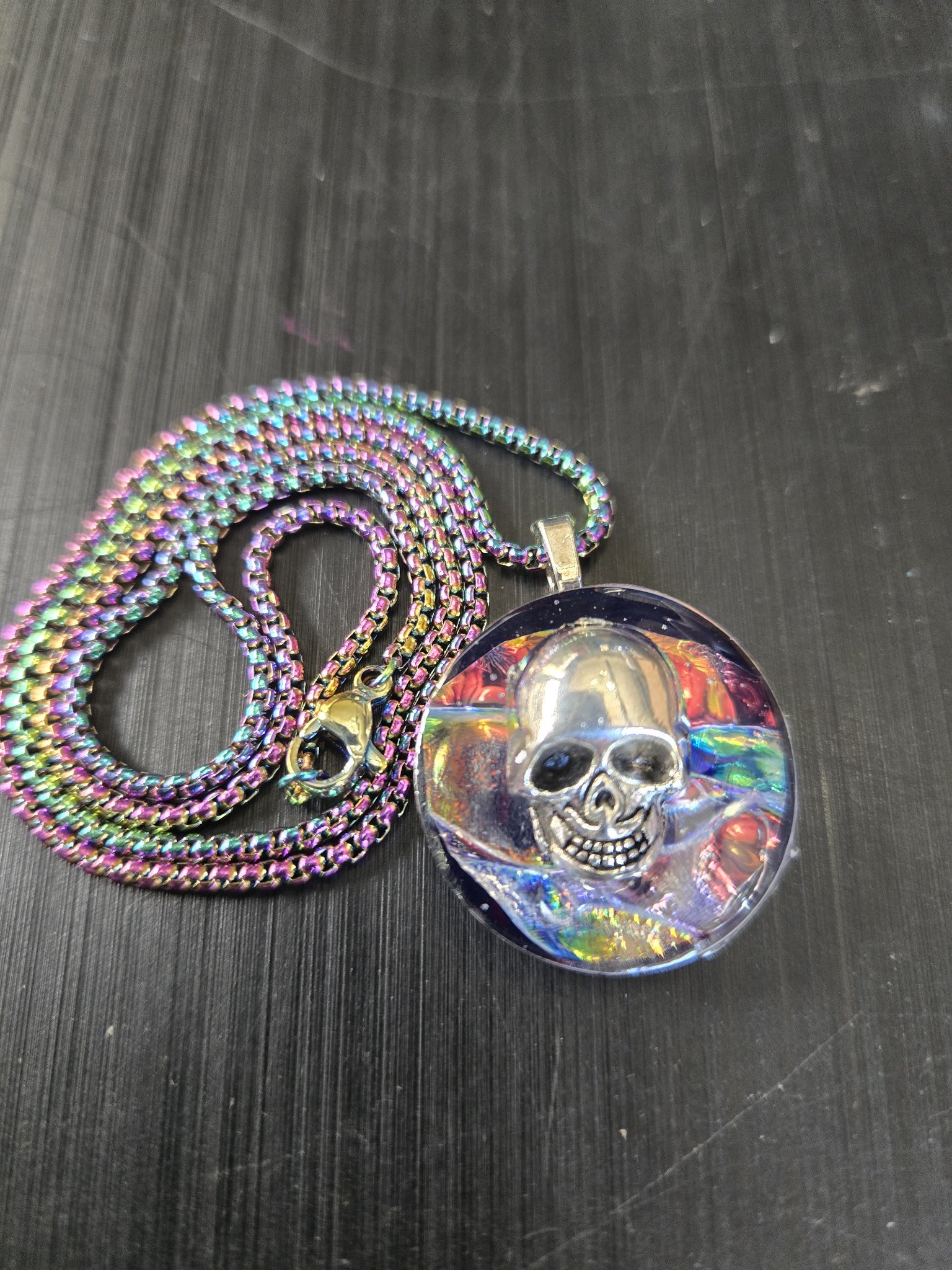 Front close-up of stock 192 round rainbow-iridescent holographic resin pendant with a silver-tone skull charm