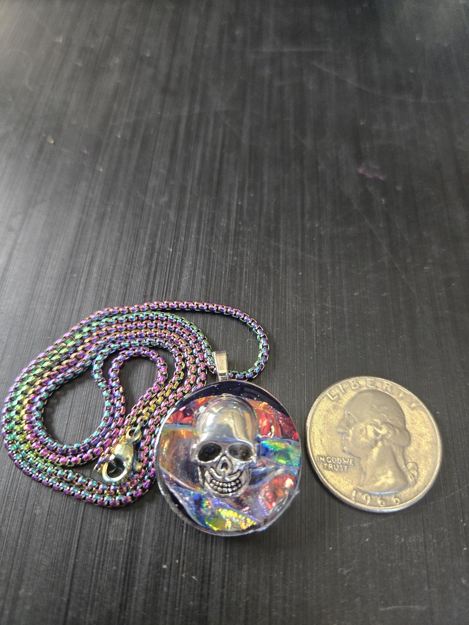 Front of stock 192 holographic skull resin pendant beside a quarter for scale