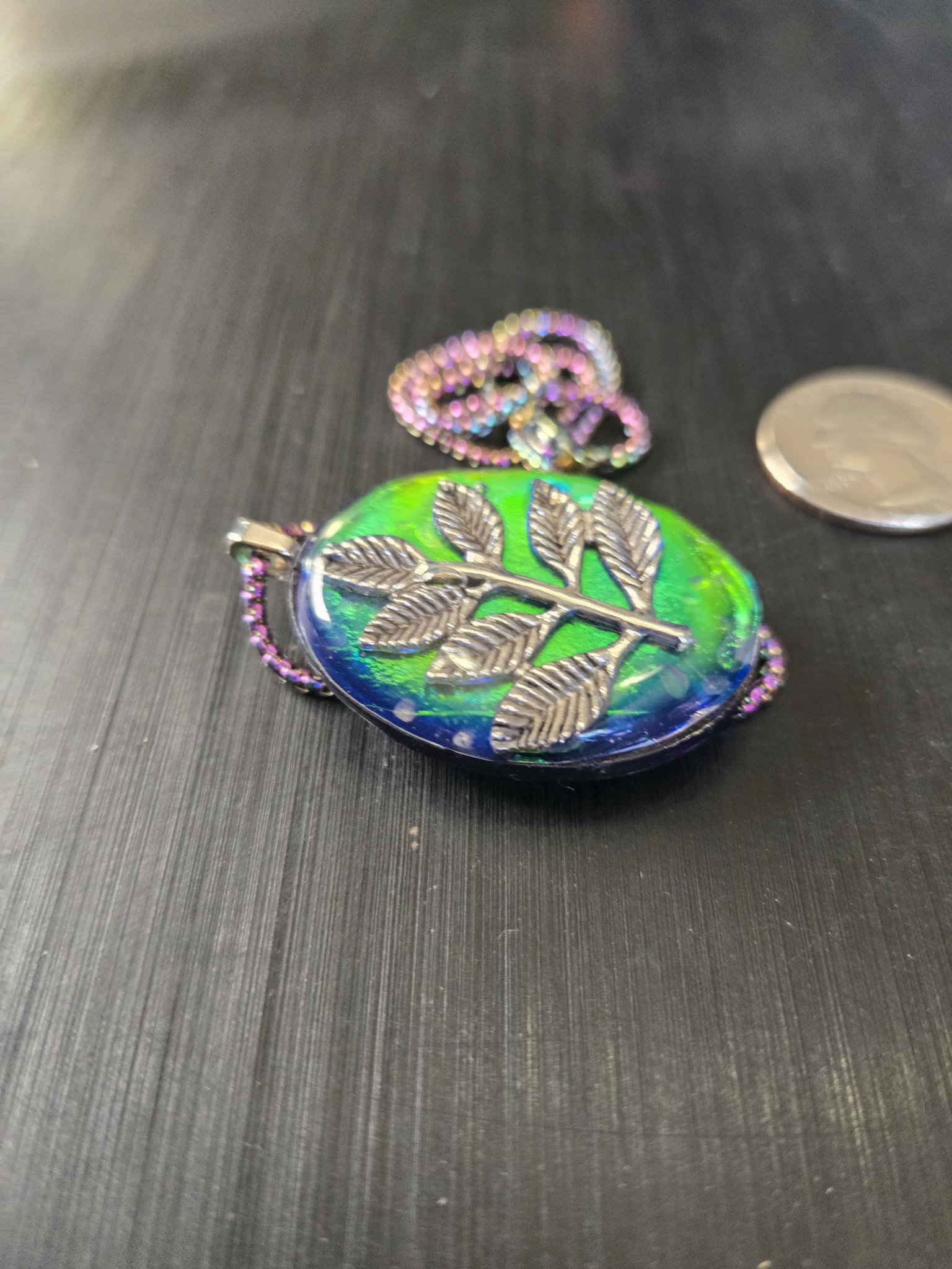 Alternate angle of stock 193 holographic branch resin pendant beside a quarter for scale