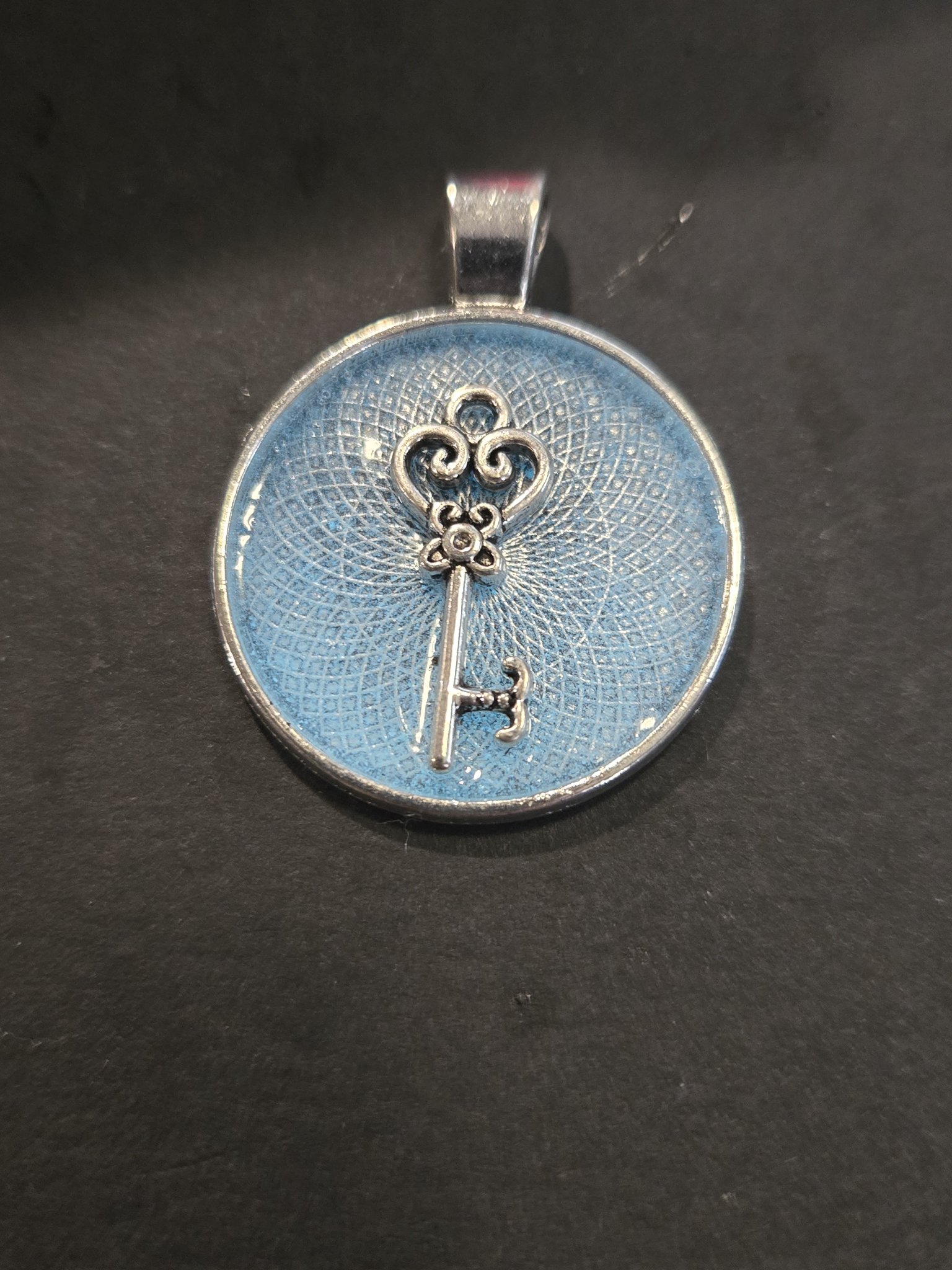 Front view of stock 202 bright blue glow-in-the-dark key resin pendant with a silver-tone ornate skeleton key charm