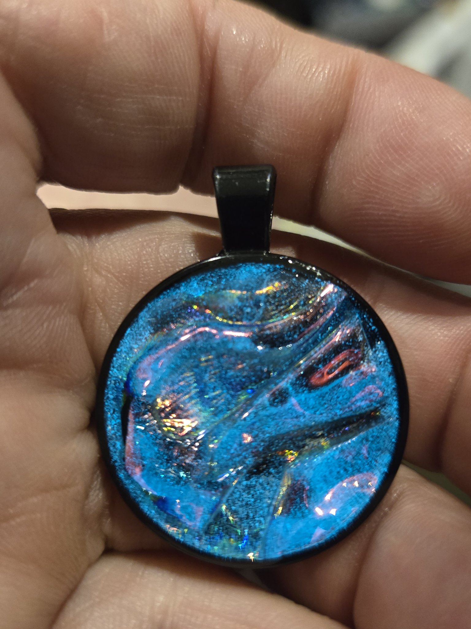 Alternate in-hand front view of stock 204 blue holographic resin pendant with rainbow swirls