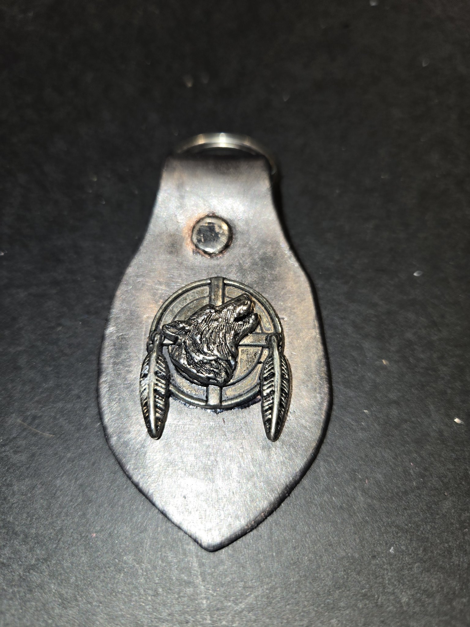 Stock 236 antiqued black leather keychain with a silver-tone shield showing a howling wolf head framed by two feathers, shown with its silver-tone rivet and split key ring