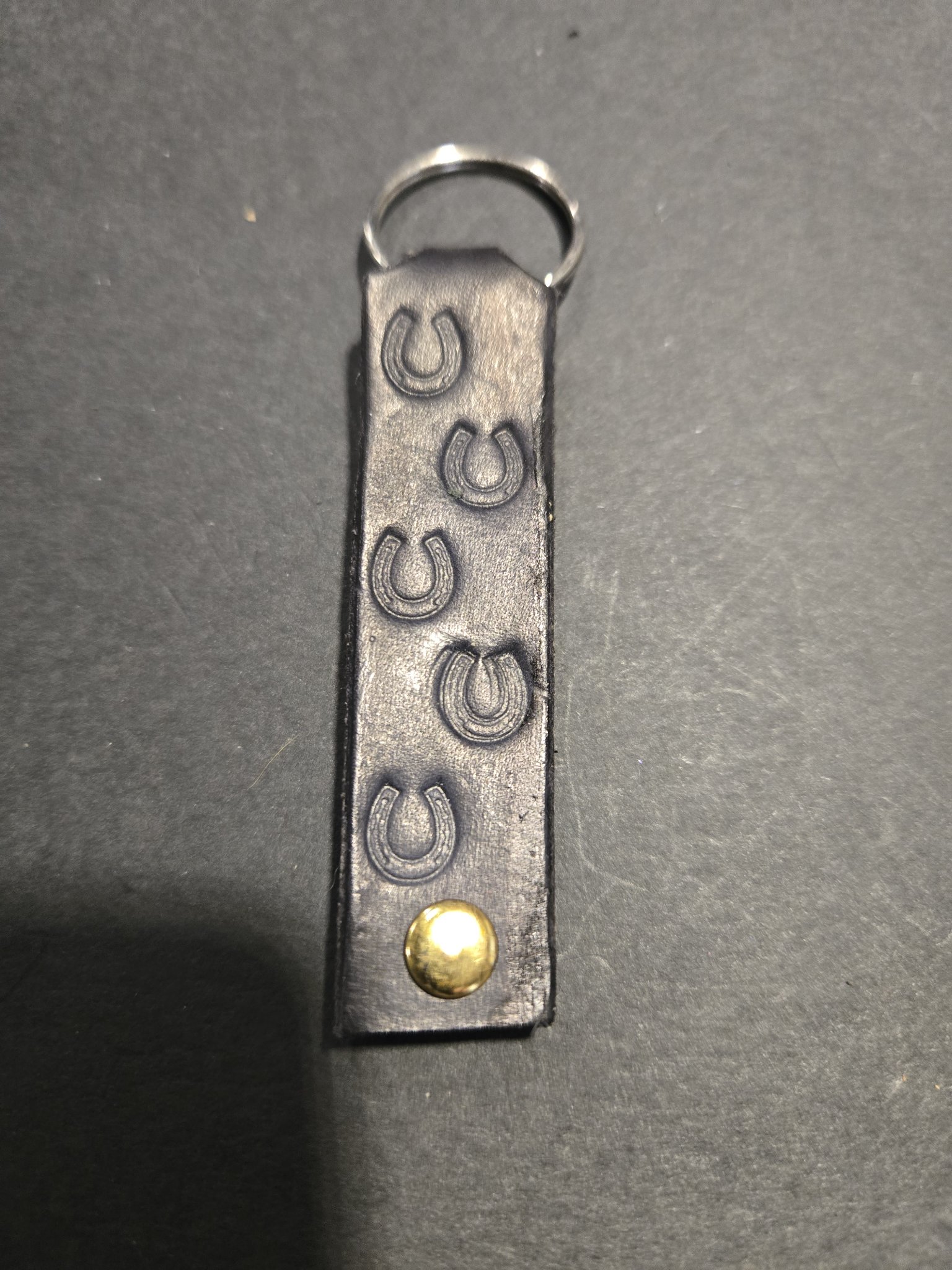 Stock 240 black leather keychain hand-stamped with horseshoes down its length, shown with its gold-tone rivet and split key ring