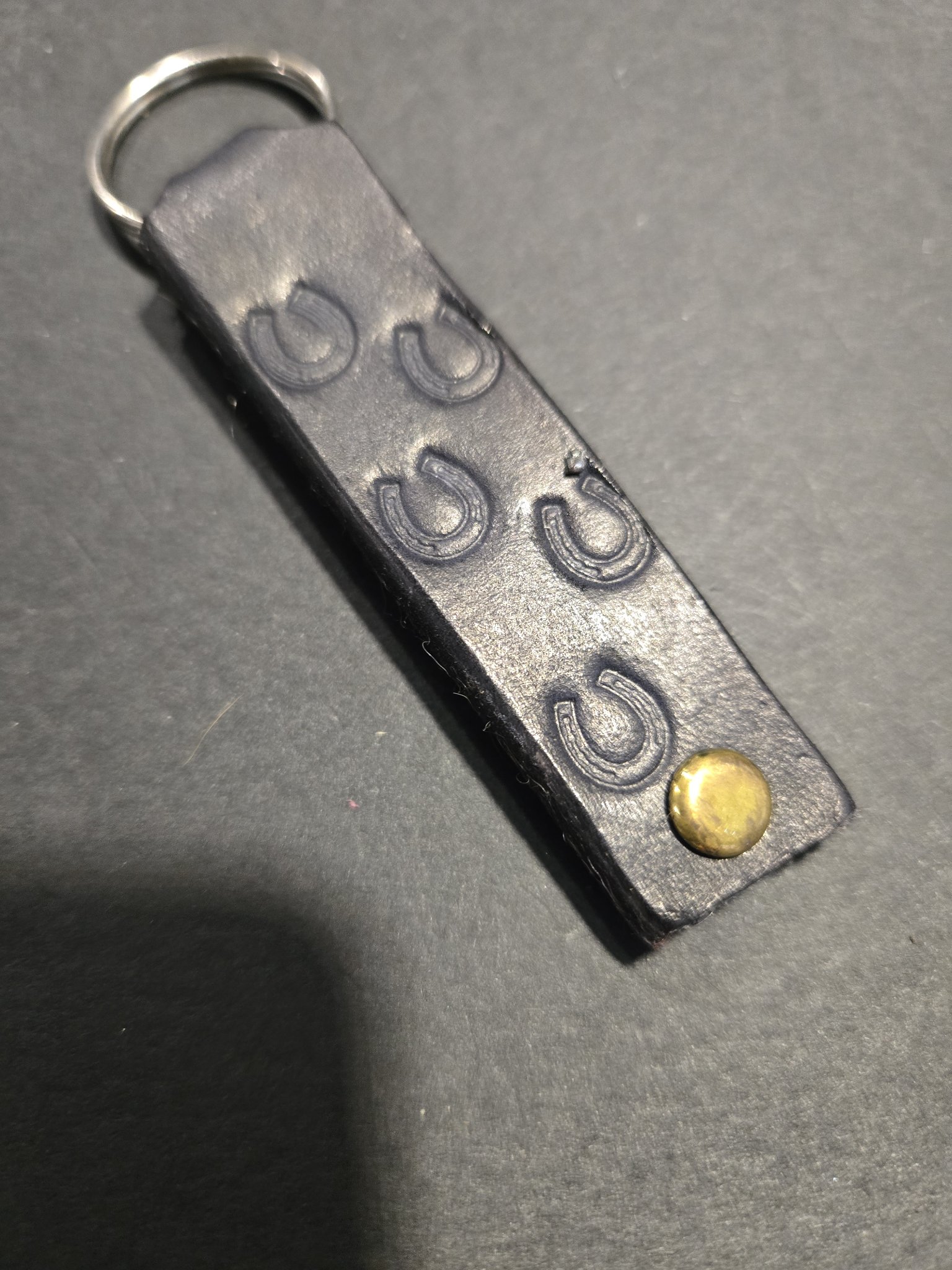 Angled view of stock 240 showing the hand-stamped horseshoes and gold-tone rivet on the black leather strap