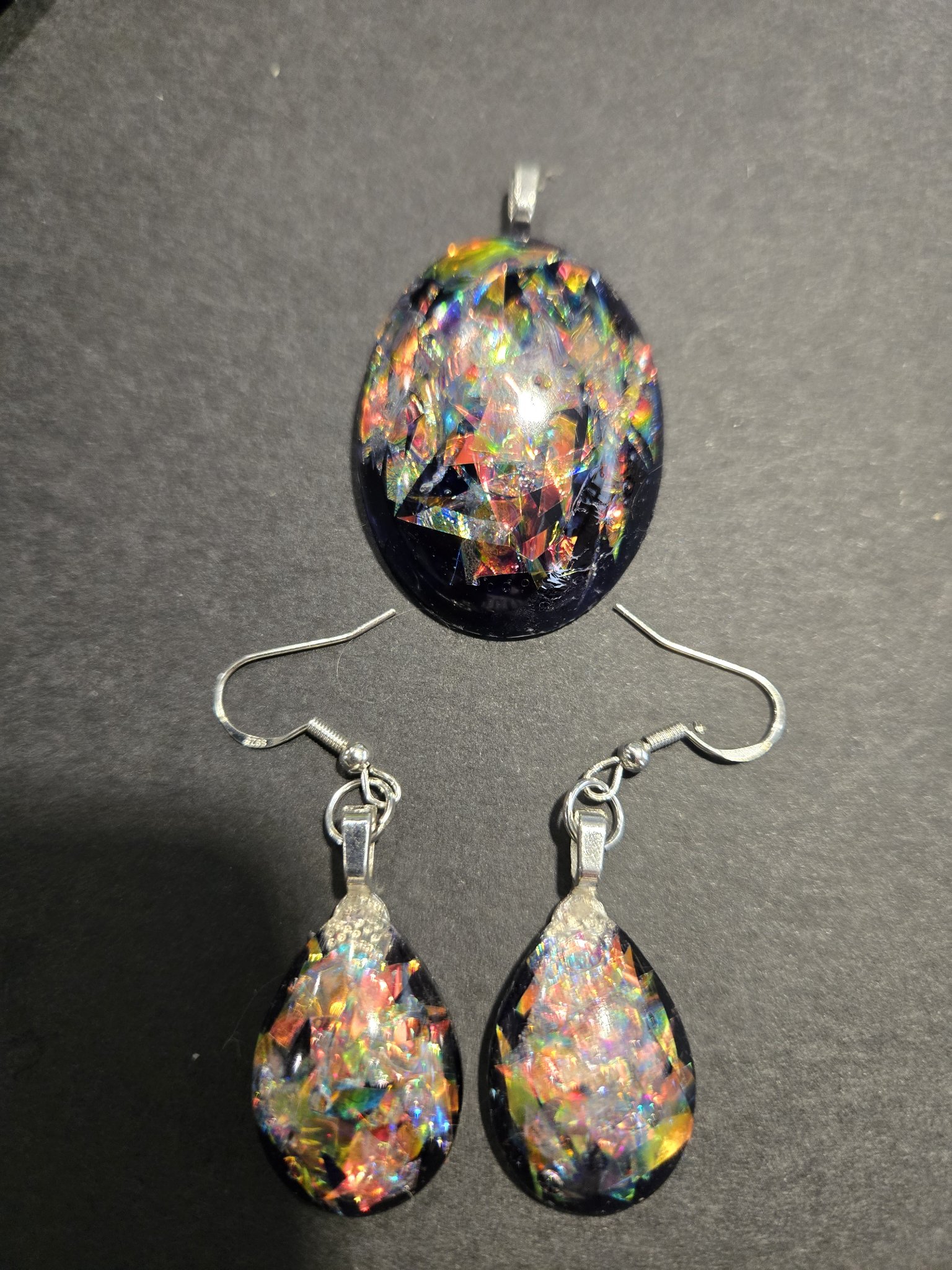Stock 249 holographic teardrop earrings and oval pendant set — black resin pieces filled with rainbow holographic flakes, the oval pendant above the matching teardrop earrings on sterling silver wires