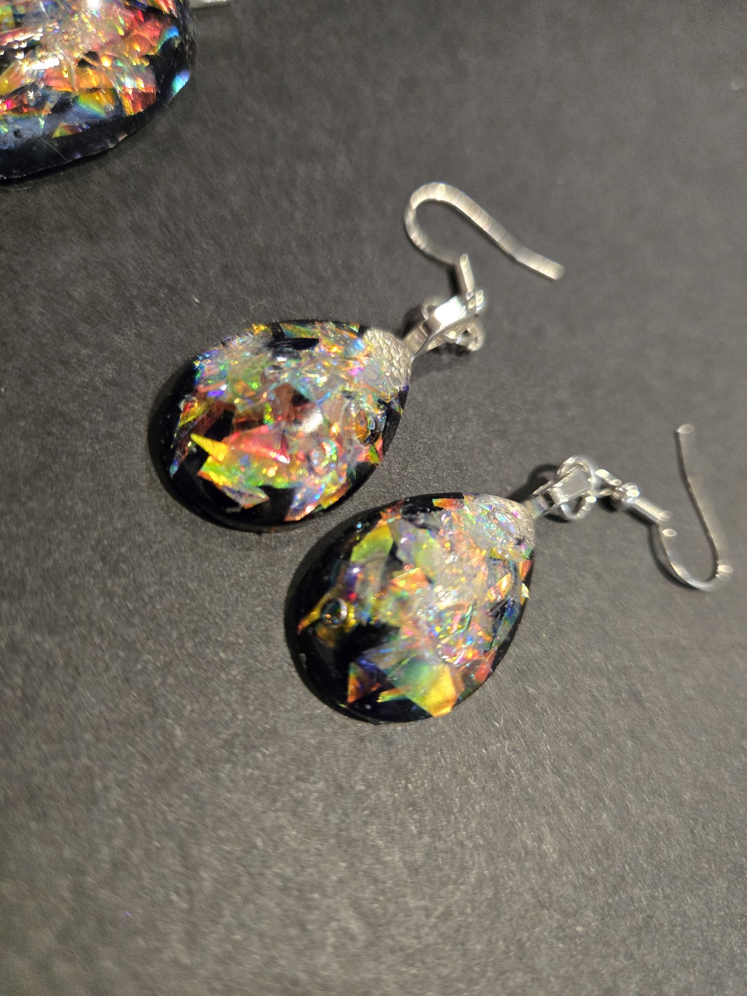 Close-up of the stock 249 holographic teardrop earrings on sterling silver wires, showing the rainbow holographic flakes against the black resin