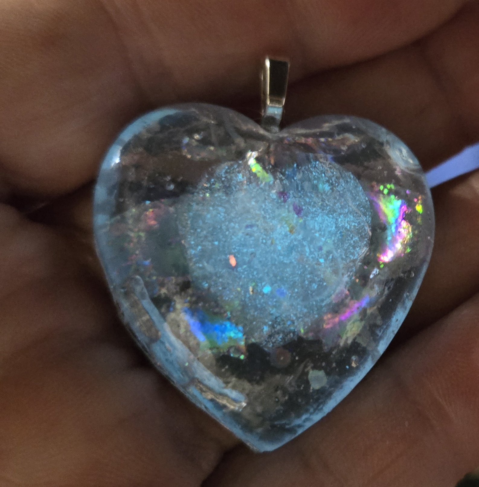 Close-up of stock 250 holographic glow heart pendant held in a hand, showing the holographic flecks in detail