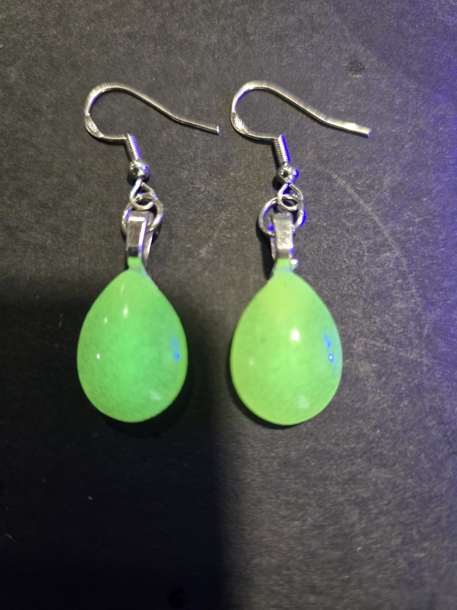 Stock 252 teardrop earrings on a dark background, glowing green