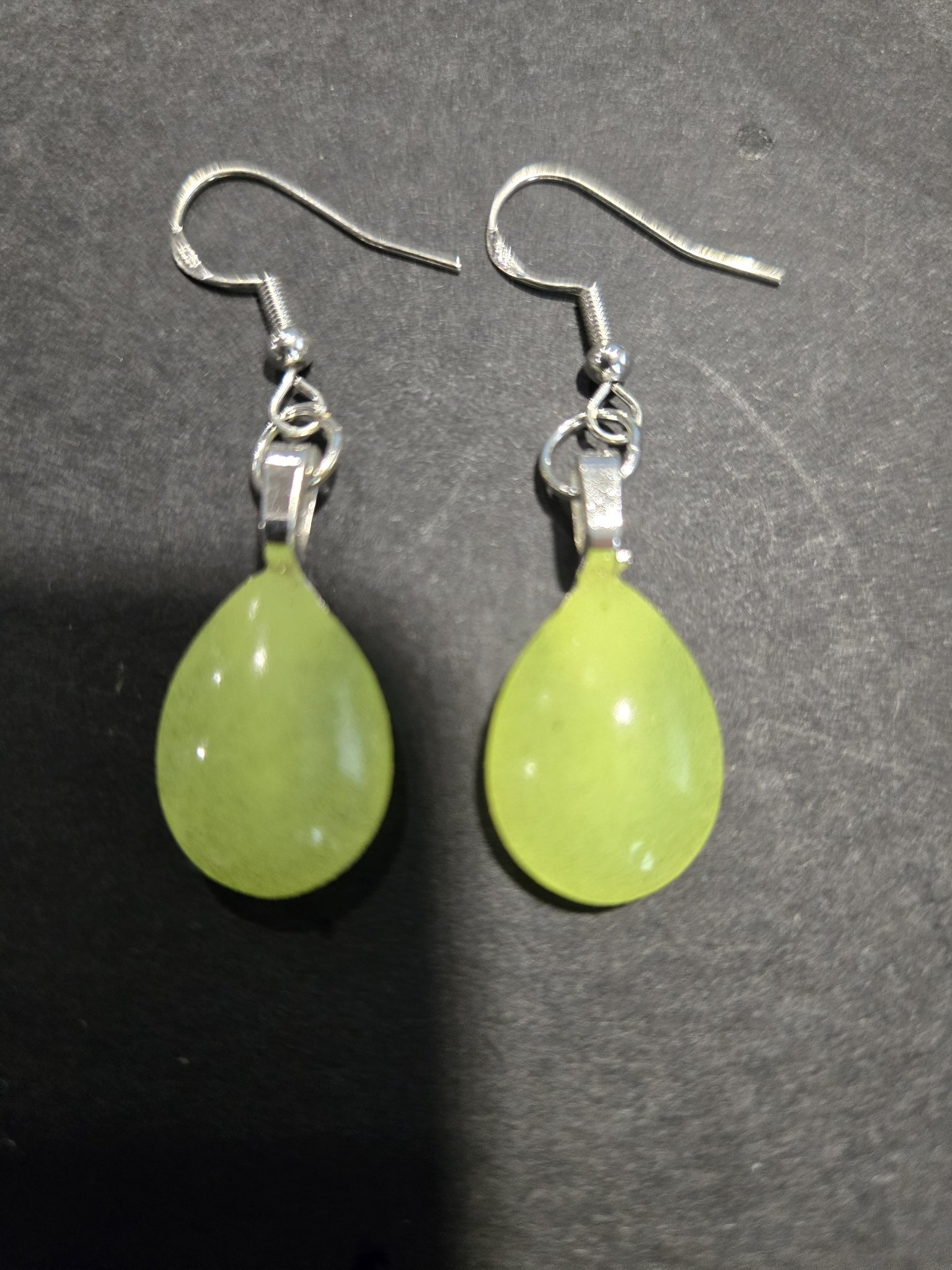 Stock 252 teardrop earrings on a dark background in normal light, showing their soft pale green color