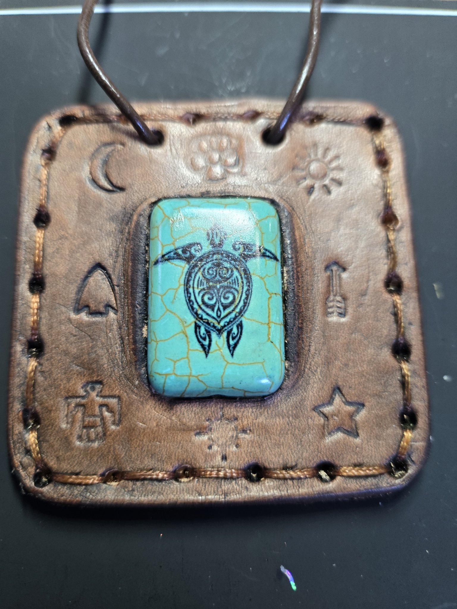 Alternate front view of the leather turtle pendant showing the hand-sewn edges and stamped designs