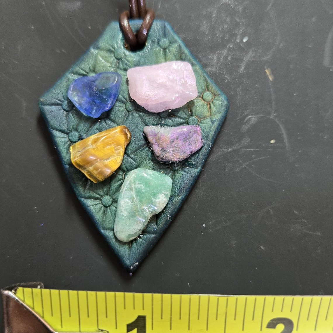 Leather and gemstone pendant beside a tape measure showing it is about two and a half inches long