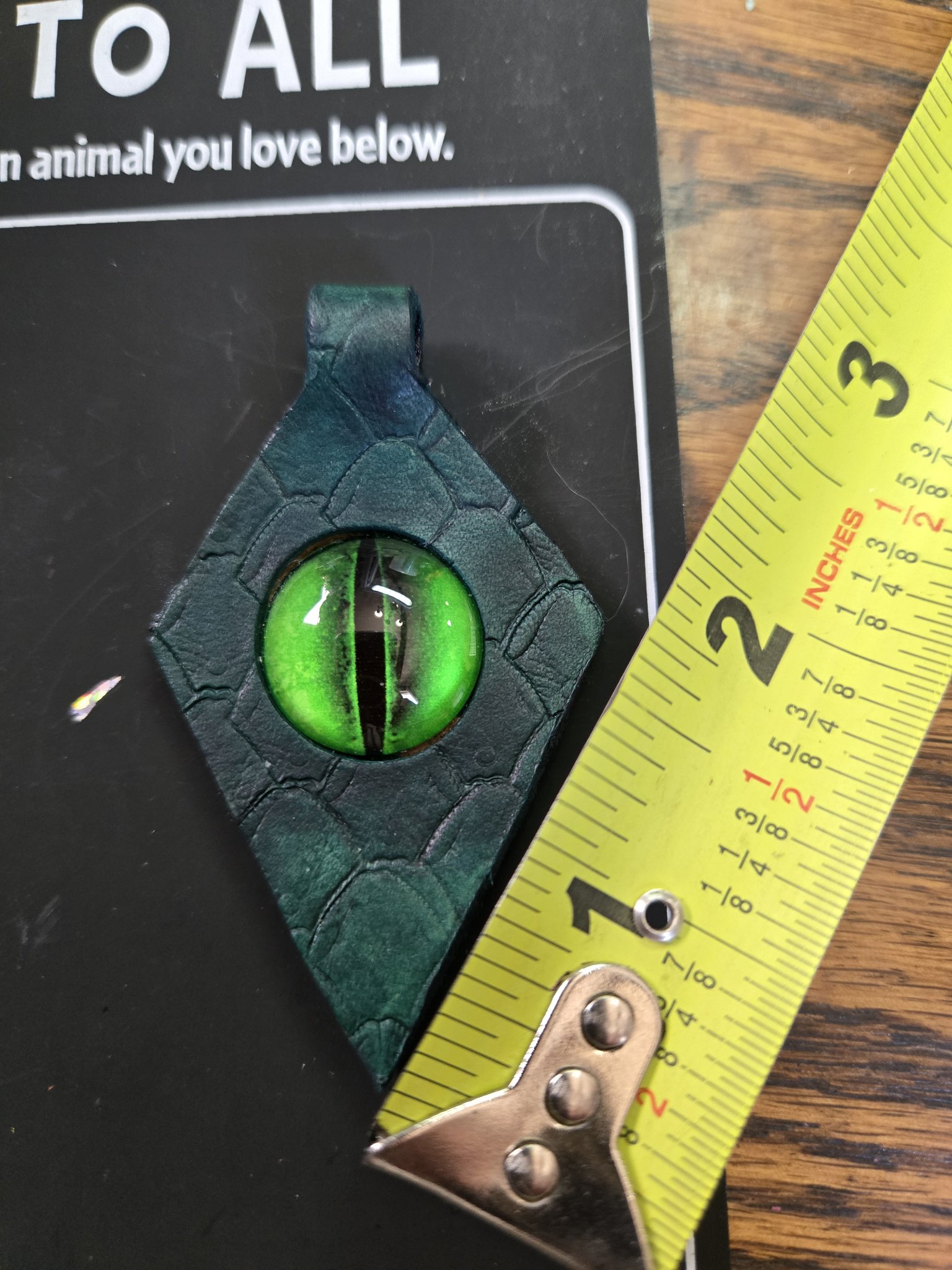 Leather green dragon eye pendant beside a tape measure showing it is about two inches long