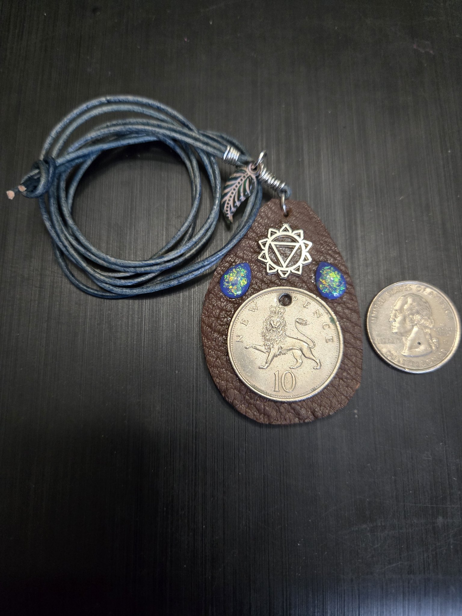 Stock 150 buffalo leather 10 pence pendant with its full blue leather cord beside a quarter for scale